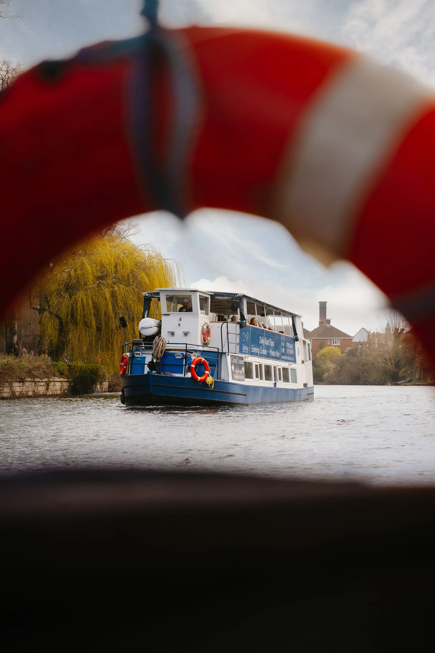 The Sabrina Boat carrying passengers along the River Severn in Shrewsbury, with the open green space of Shrewsbury Quarry visible in the background in Shropshire.