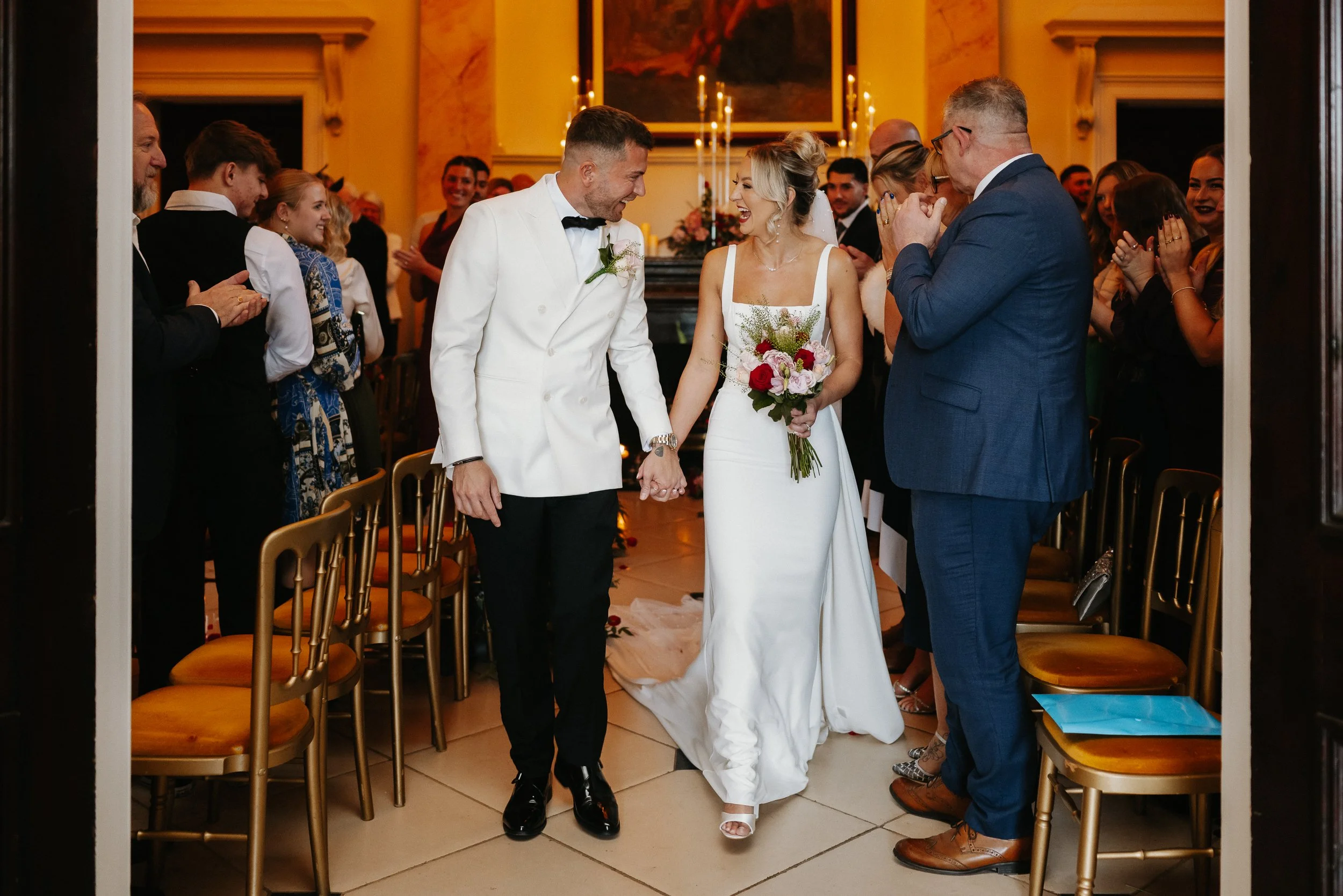 Bride and groom walking back down the aisle at Netley Hall after their winter wedding ceremony, smiling and celebrating as guests cheer around them.