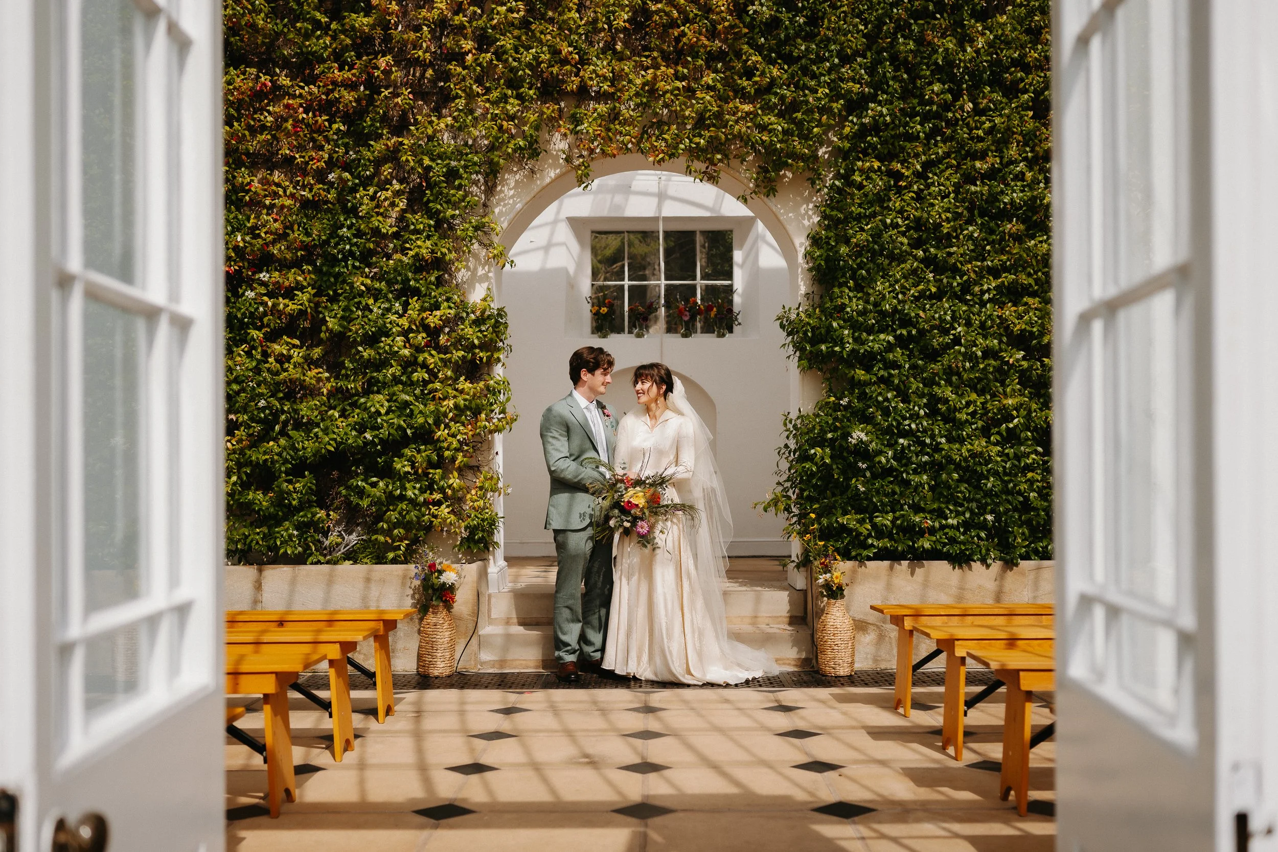 Bride and groom standing beneath the ivy covered arch inside the orangery at Hopton Court Estate in Shropshire, natural wedding portrait