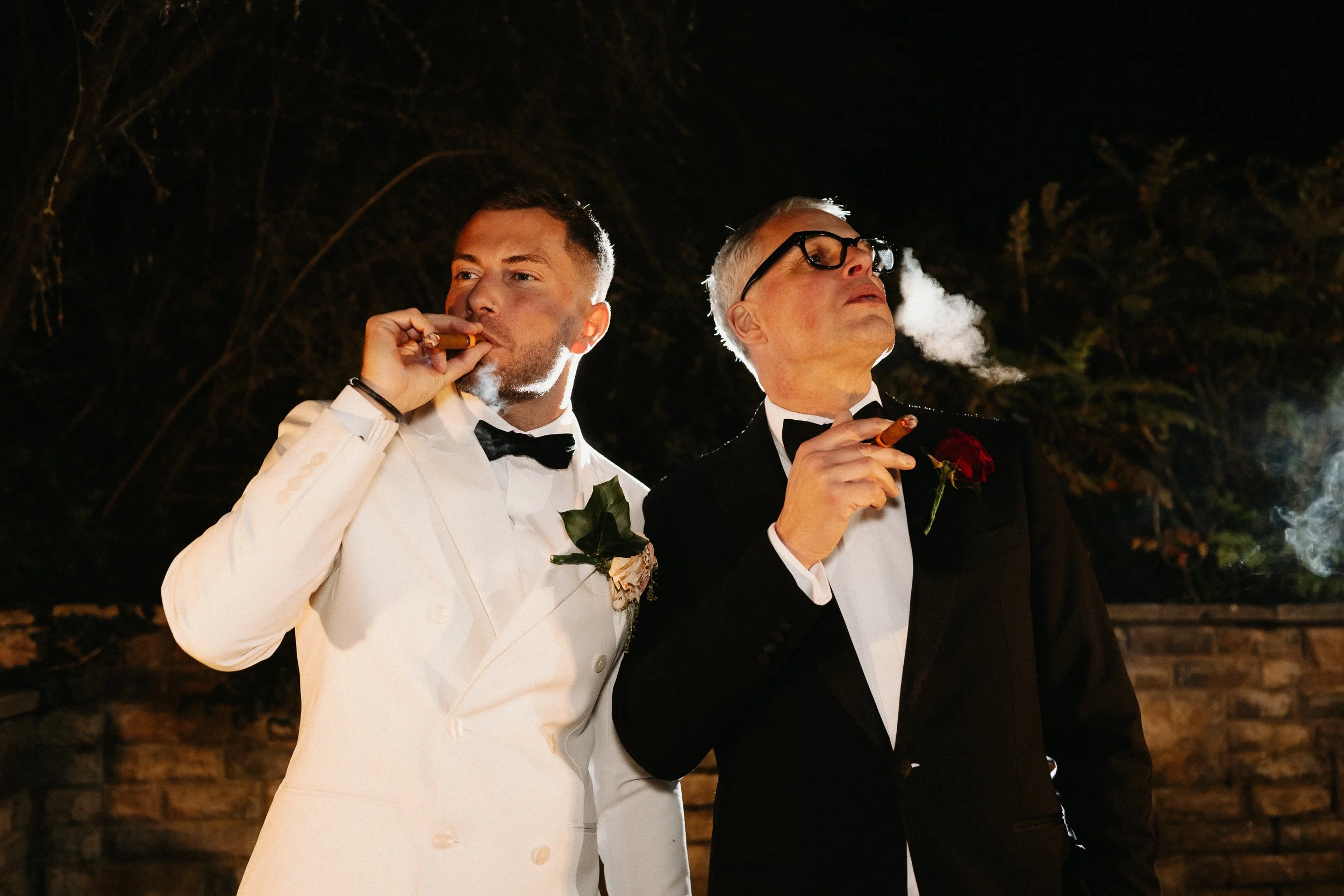 Groomsmen smoking cigars outside Netley Hall during the winter wedding reception, relaxing and chatting together.