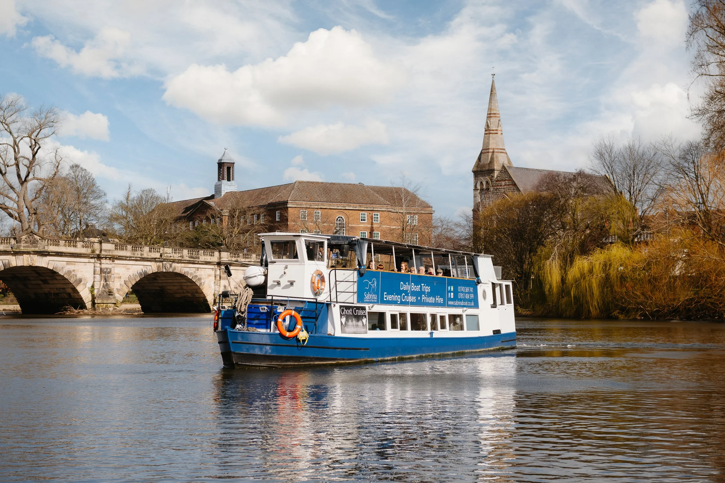 The Sabrina Boat carrying passengers along the River Severn in Shrewsbury, with the open green space of Shrewsbury Quarry visible in the background in Shropshire.