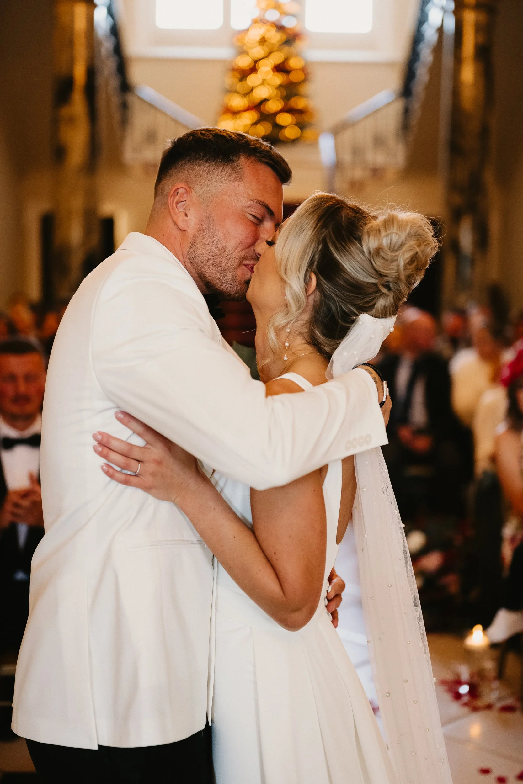 Bride and groom sharing their first kiss during their winter wedding ceremony at Netley Hall, surrounded by cheering guests.