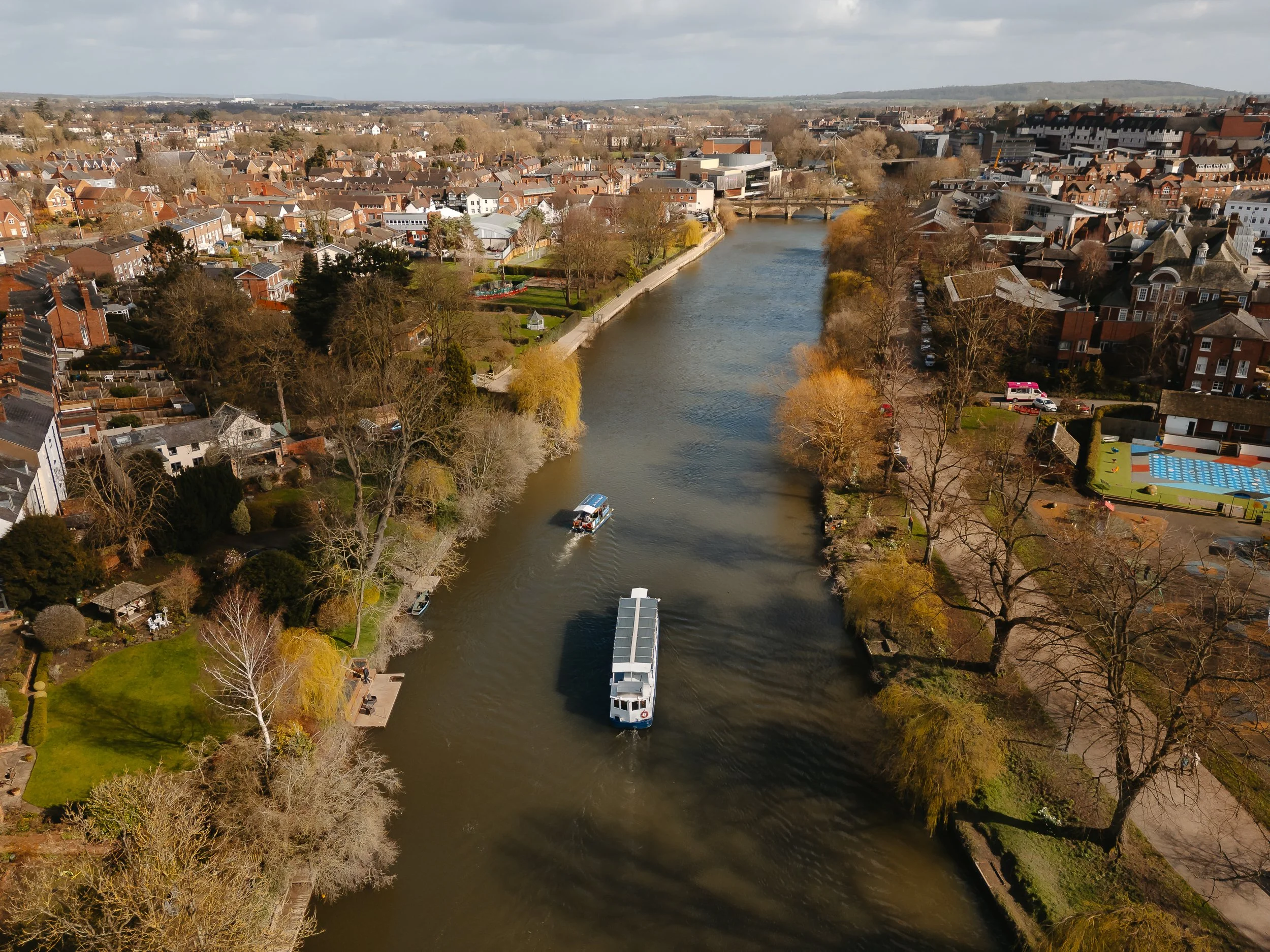 The Sabrina Boat carrying passengers along the River Severn in Shrewsbury, with the open green space of Shrewsbury Quarry visible in the background in Shropshire.