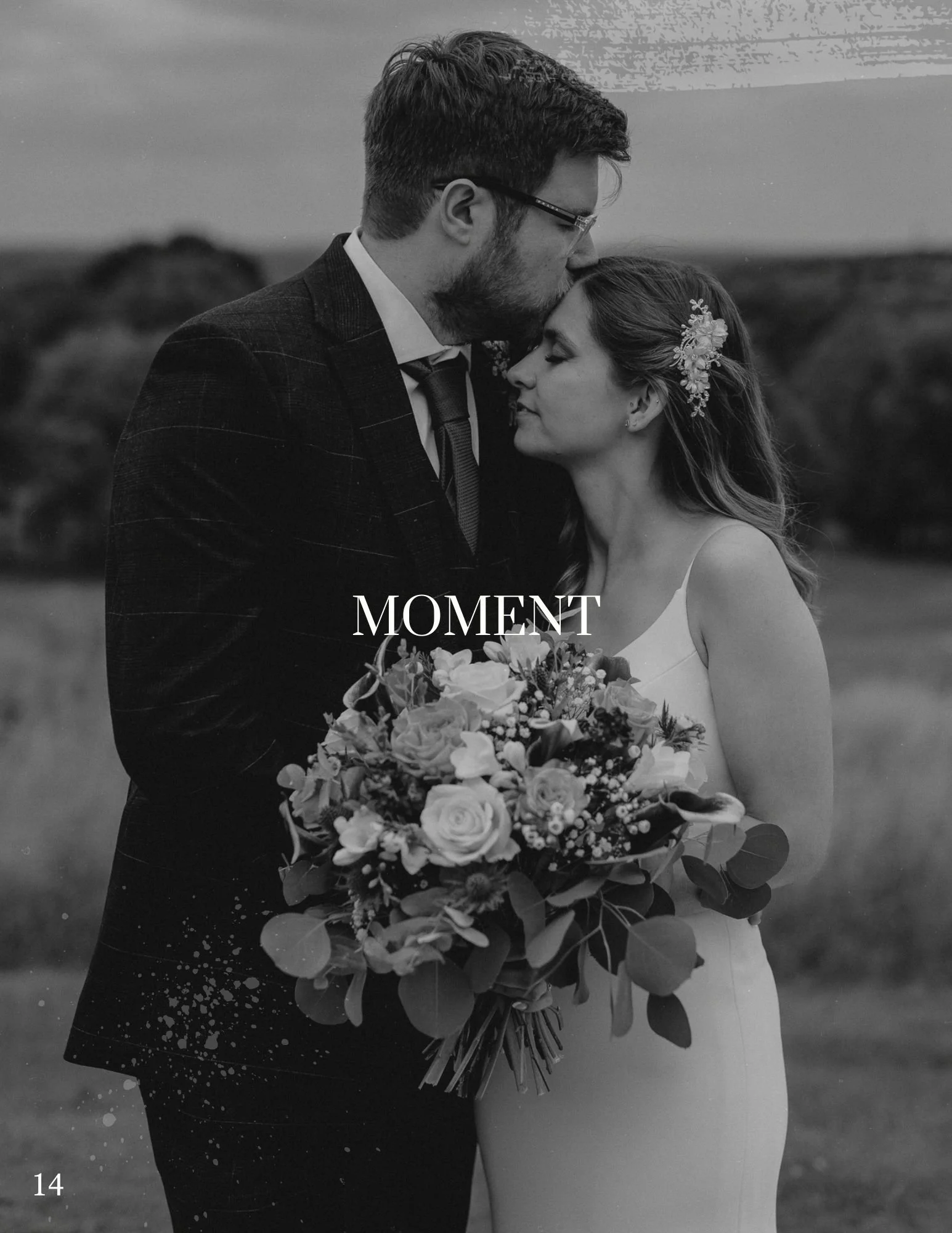 Black and white photo of a bride and groom standing outdoors. The groom is kissing the bride on her forehead while she holds a bouquet of flowers. The background is blurred with natural scenery. The word "MOMENT" is written in the center of the image