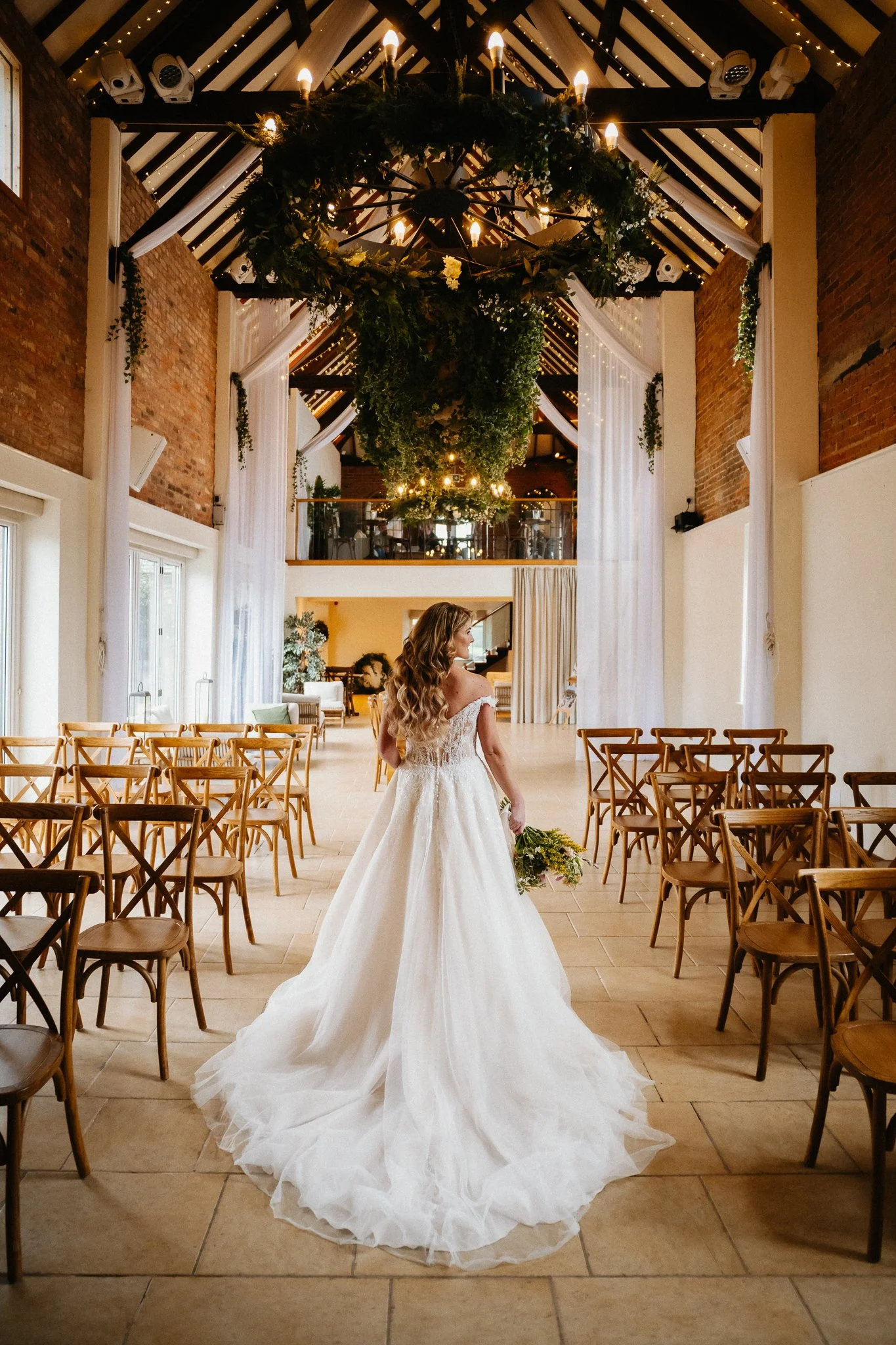 Bride photographed from behind in her long wedding dress inside the chapel at The Barns at Delbury Hall, Craven Arms.