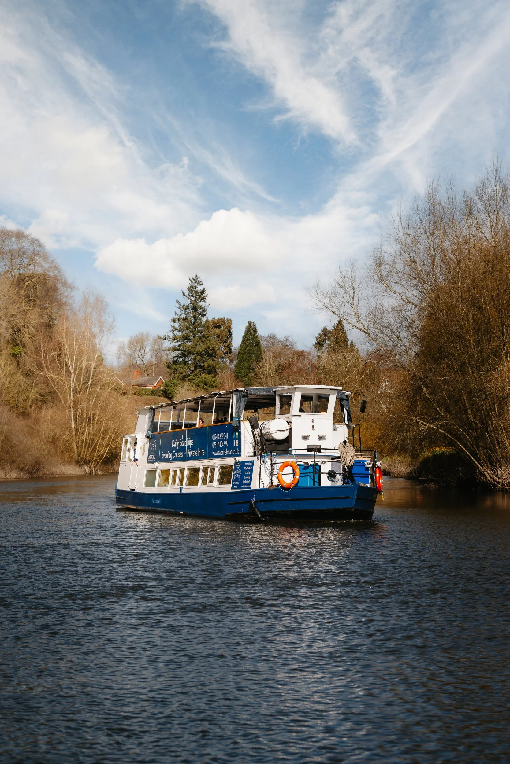 The Sabrina Boat carrying passengers along the River Severn in Shrewsbury, with the open green space of Shrewsbury Quarry visible in the background in Shropshire.