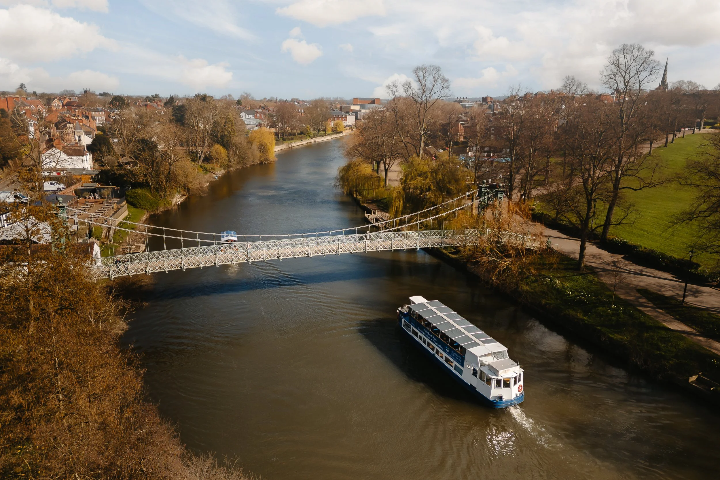 The Sabrina Boat carrying passengers along the River Severn in Shrewsbury, with the open green space of Shrewsbury Quarry visible in the background in Shropshire.