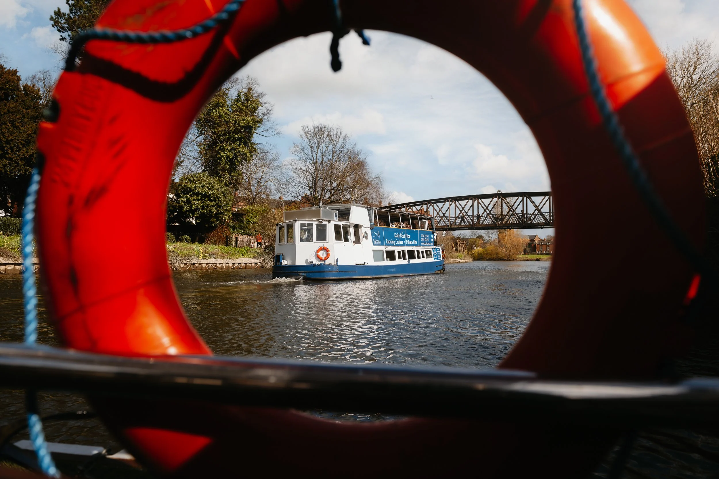 The Sabrina Boat carrying passengers along the River Severn in Shrewsbury, with the open green space of Shrewsbury Quarry visible in the background in Shropshire.