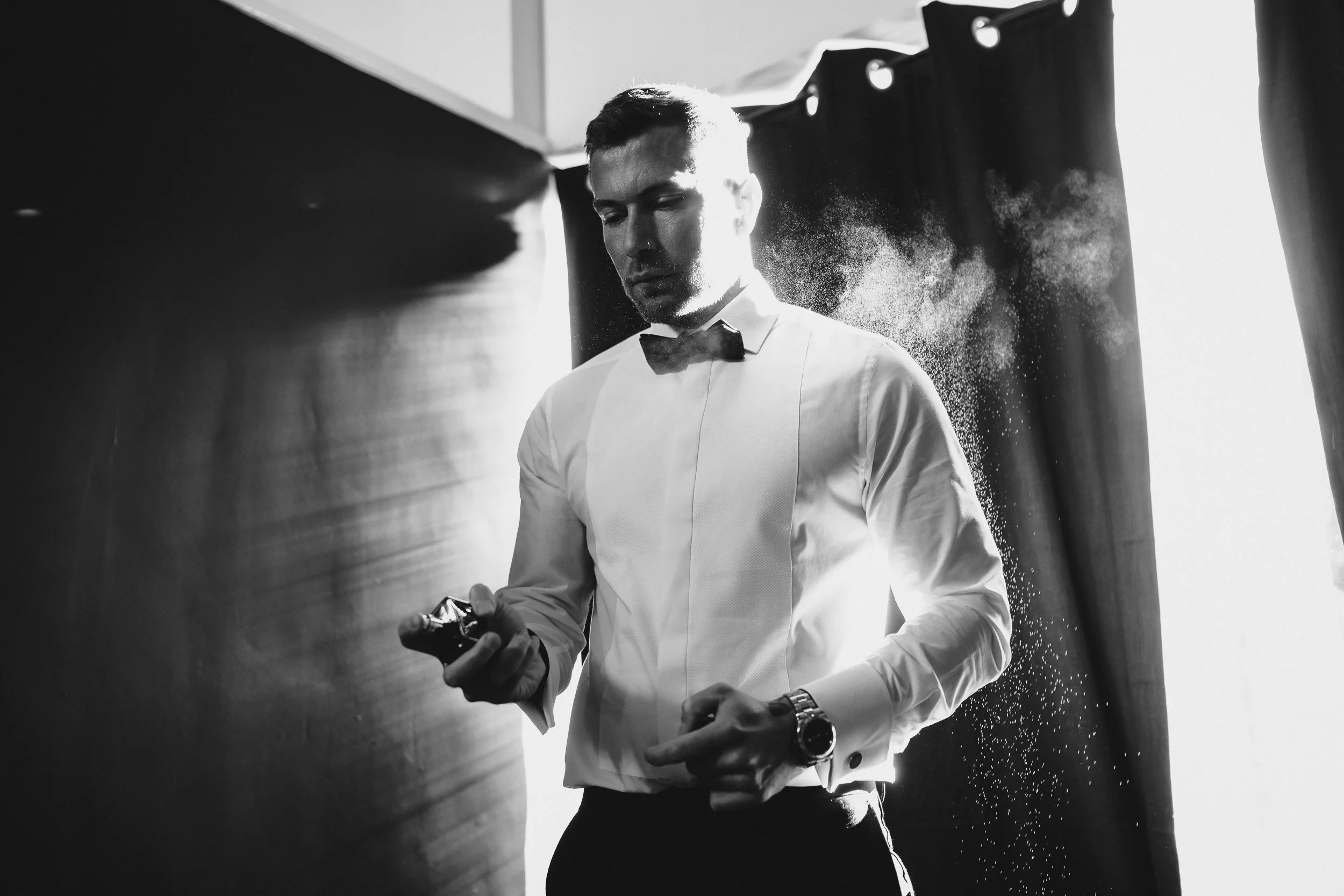 Groom spraying aftershave while getting ready at Netley Hall winter wedding