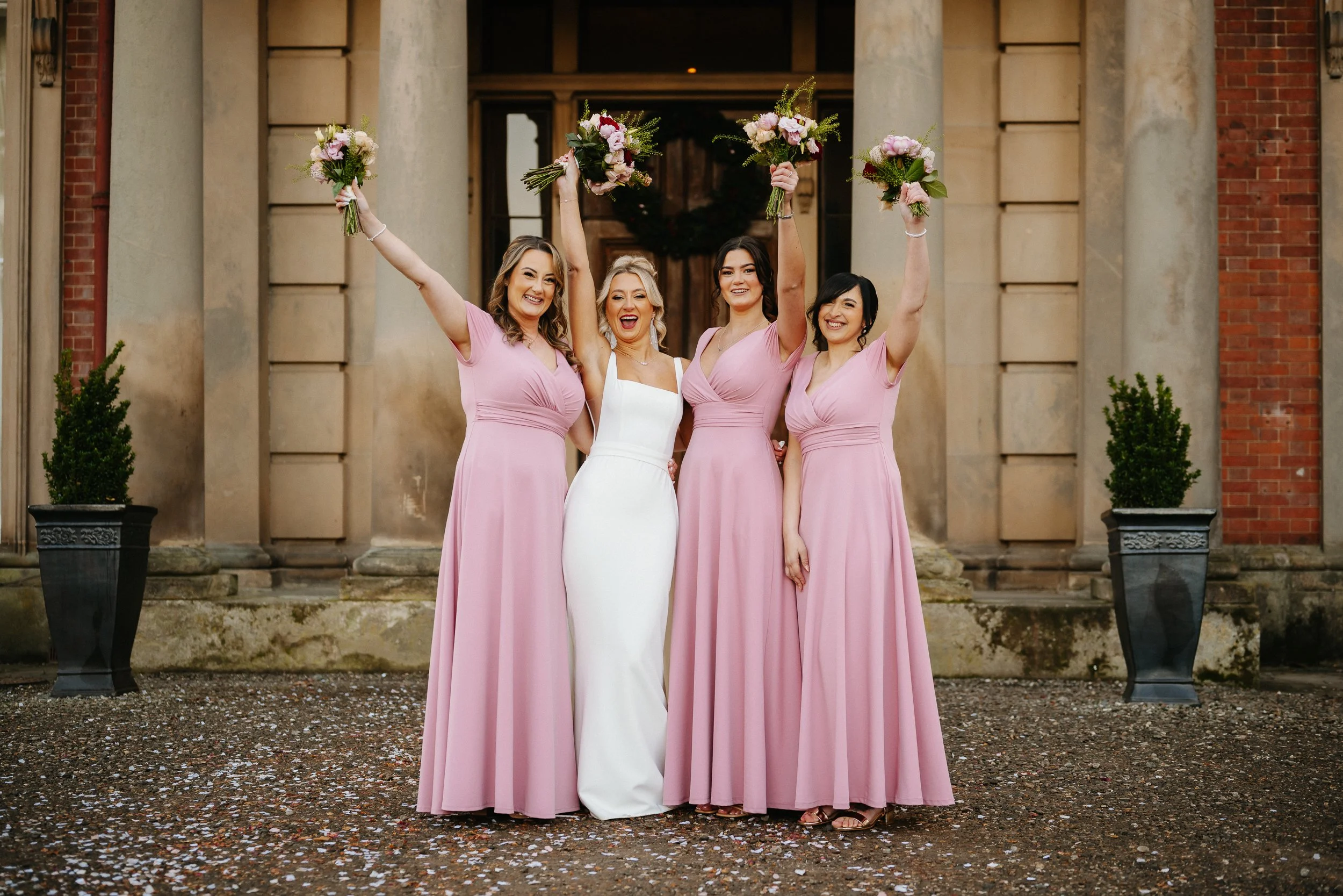 Bridesmaids posing together and smiling outside Netley Hall during a winter wedding group photo.