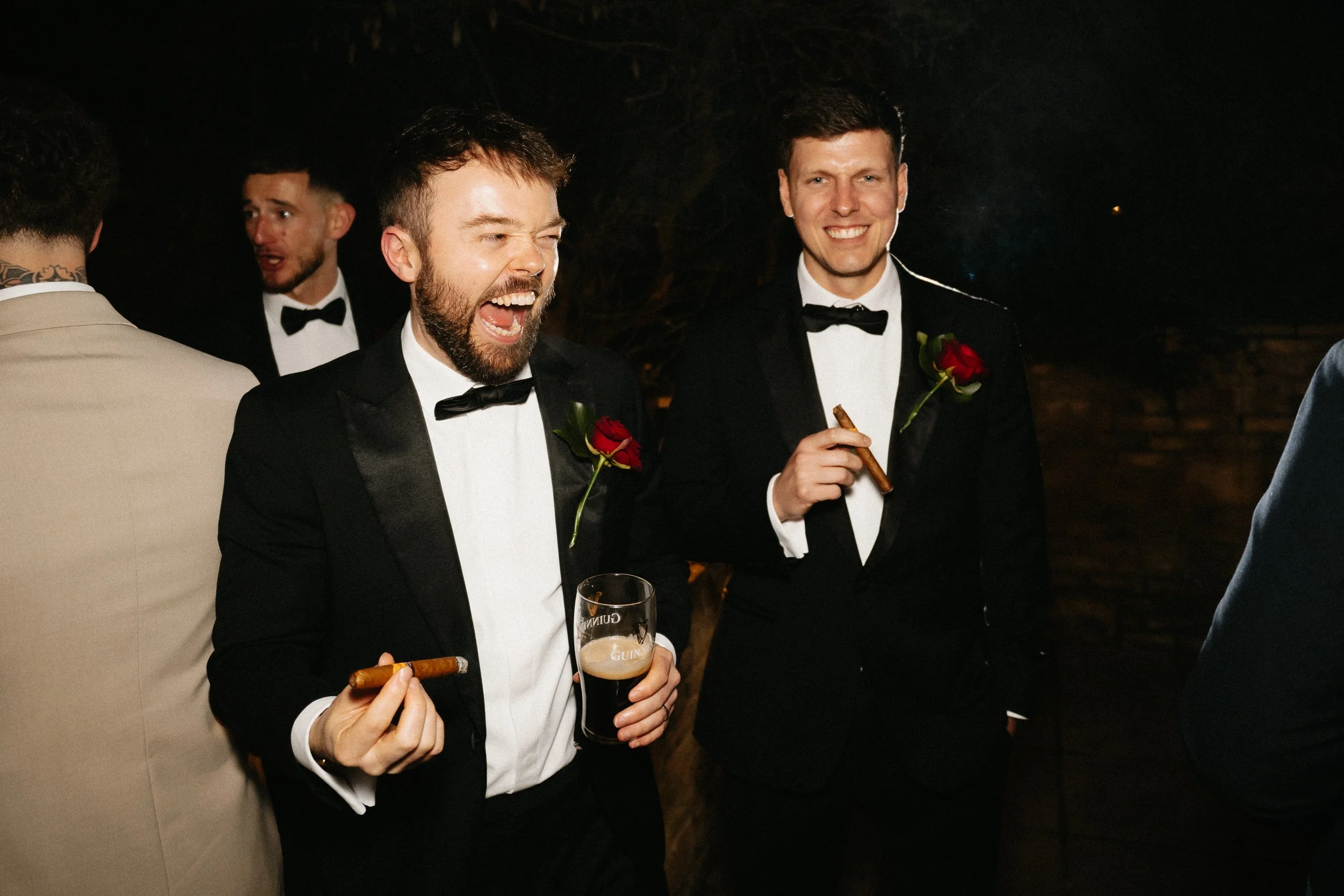 Groomsmen smoking cigars outside Netley Hall during the winter wedding reception, relaxing and chatting together.