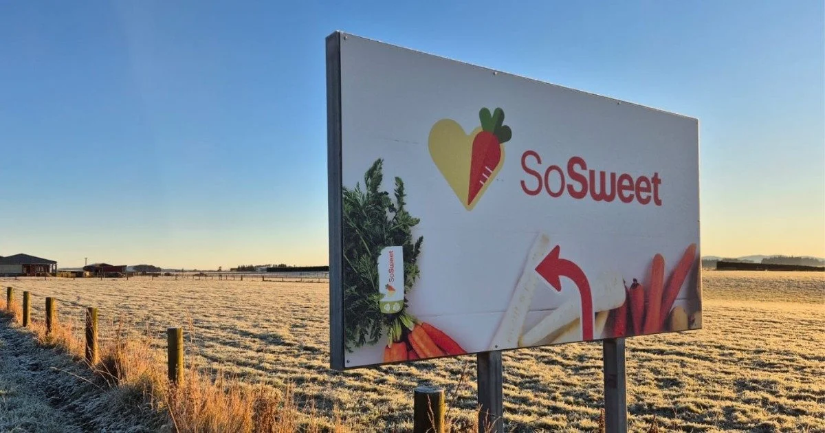 Billboard advertising So Sweet, with images of a leaf, a carrot, and other vegetables in a field at sunset.