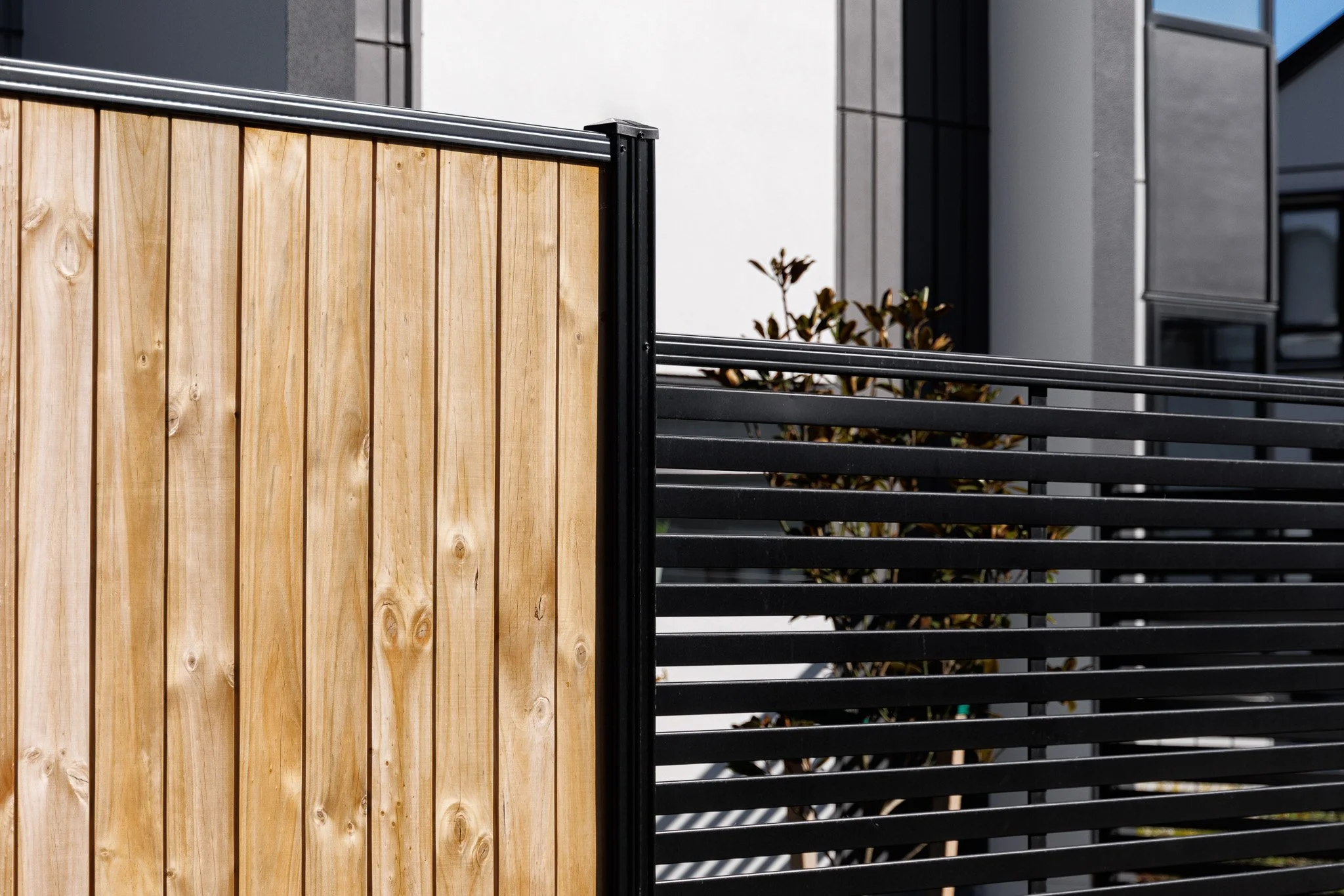 Close-up of a modern exterior fence with contrasting wood and black metal panels created by Boundaryline Fence Systems, with a small plant in the background.