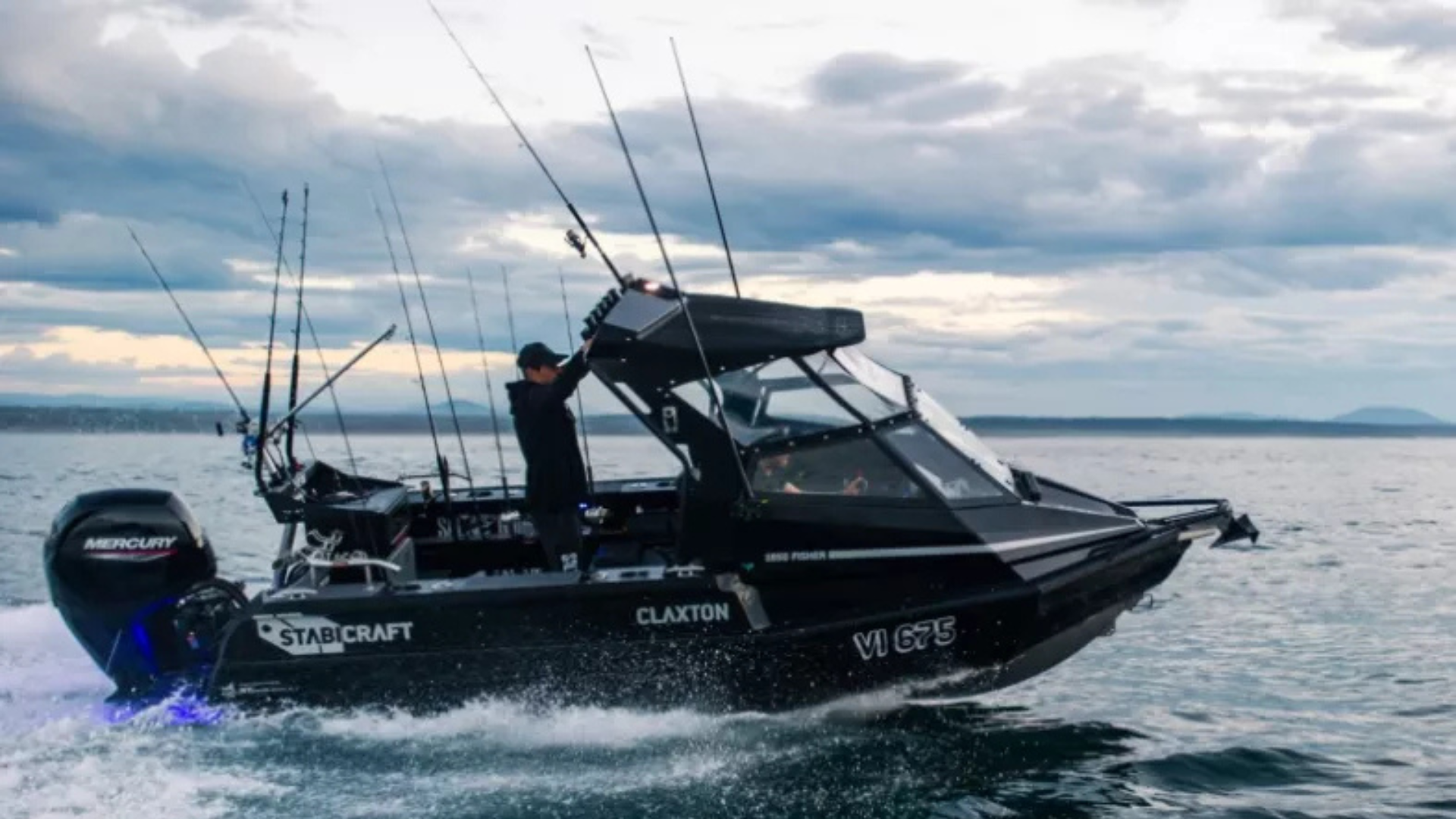 Black Stabicraft  with fishing rods on the boat, moving on the water under cloudy sky, with a person standing and adjusting equipment