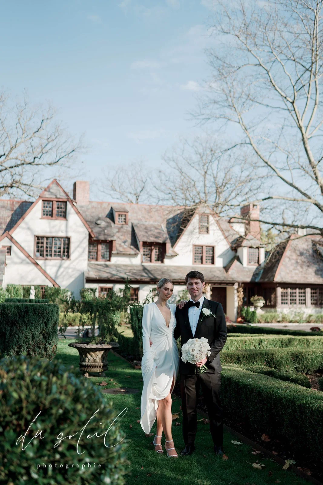 Bride and groom in a formal garden in front of a historic inn