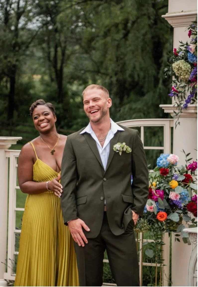 Two wedding guests laughing beside a flower-covered arbor