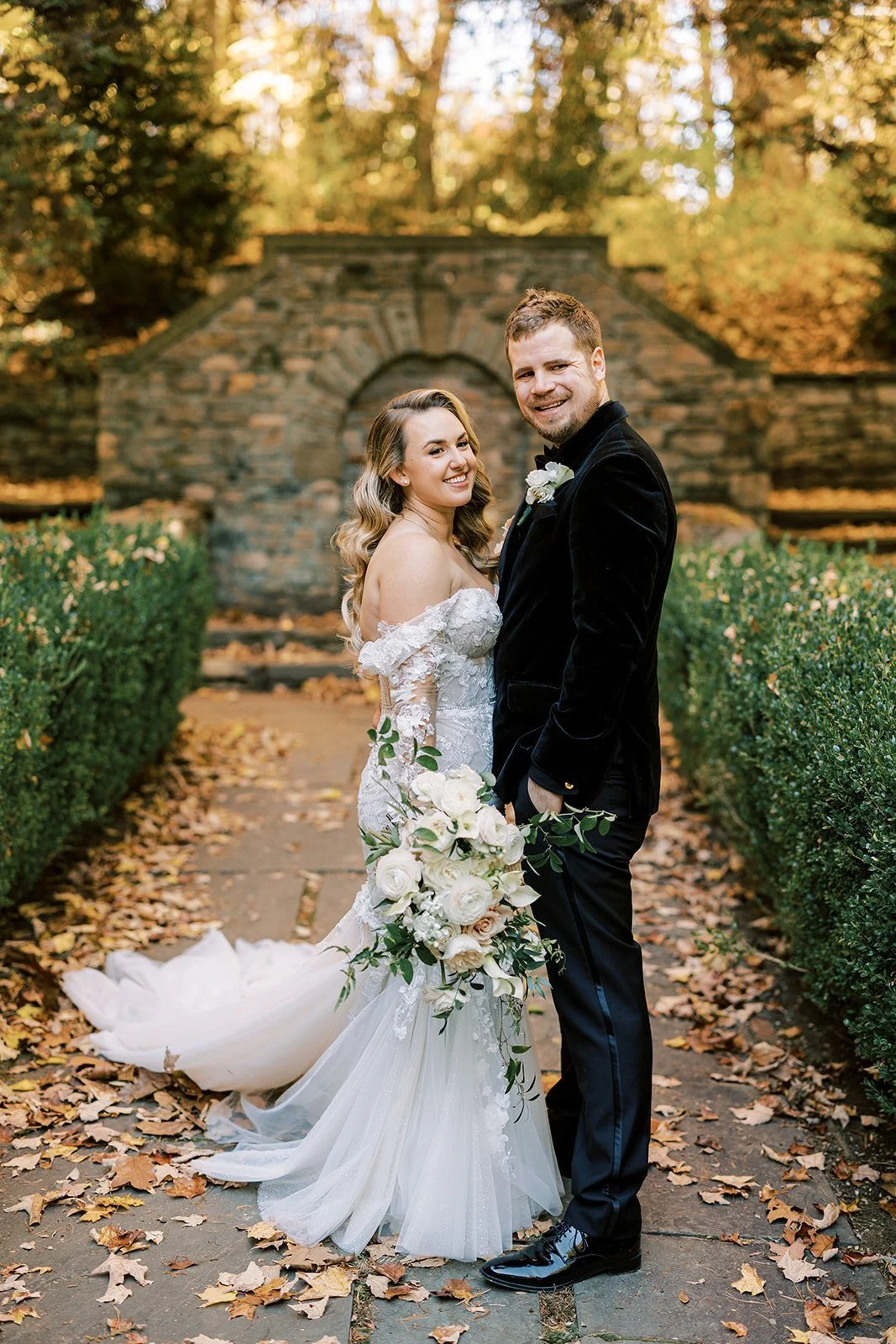 Bride and groom on a leaf-covered garden path in autumn