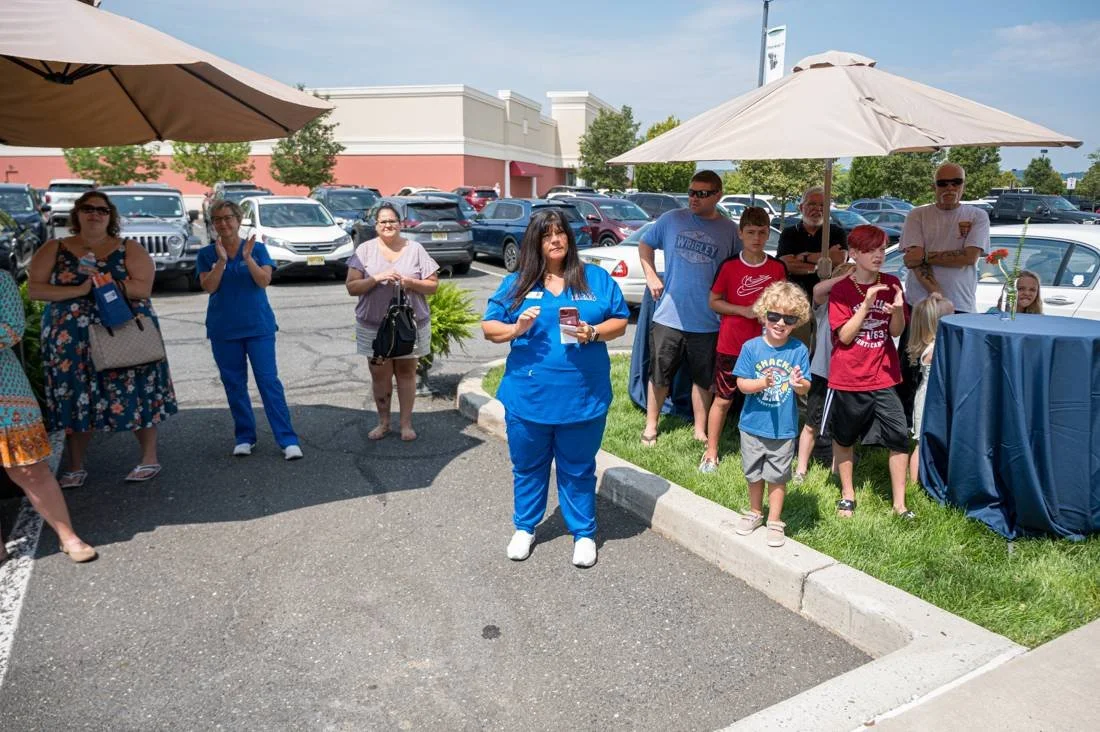 Families gathered outside at a grand opening, with a staff member in blue scrubs at the center