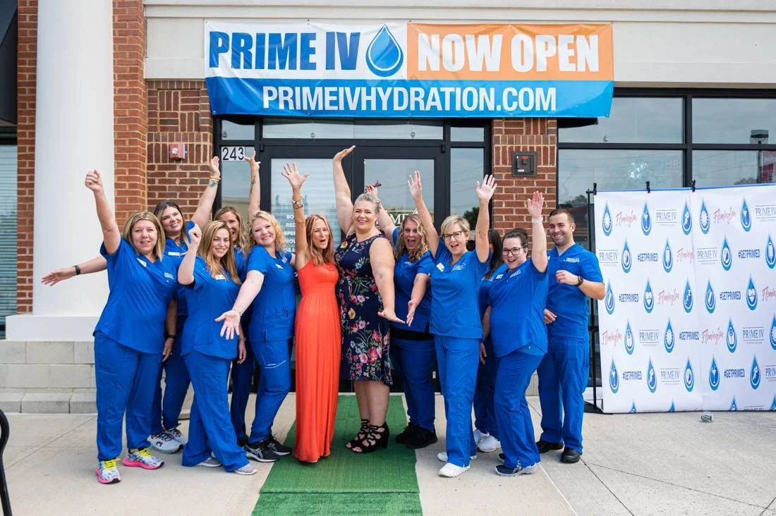 Opening day team in blue scrubs cheering with arms raised outside their storefront