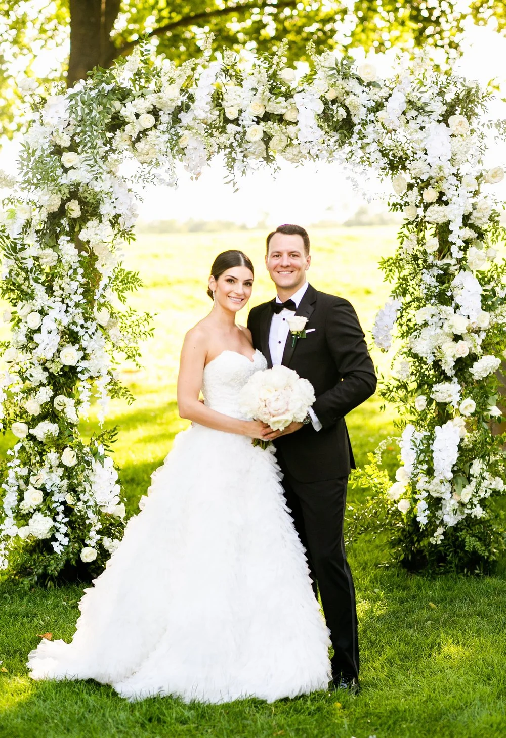 Bride and groom under a white floral arch