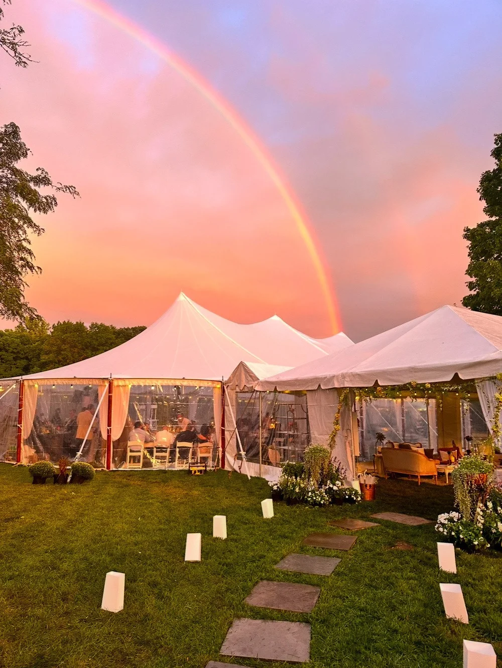 Sailcloth tent glowing under a rainbow at sunset