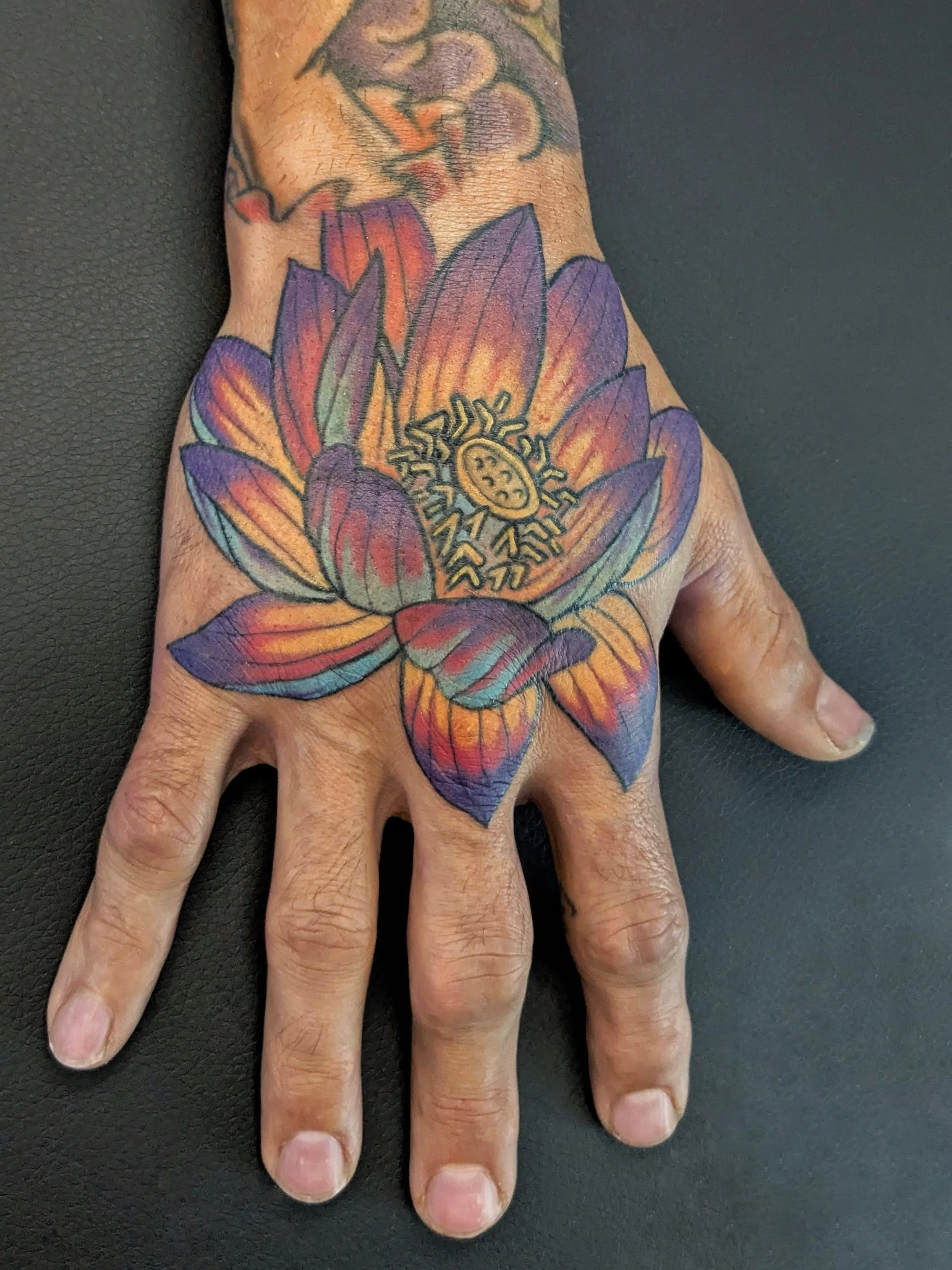 a colorful lotus tattoo on a hand done by Carlyn Crispell at Goat Witch Tattoo, a tattoo shop in Boulder, Colorado