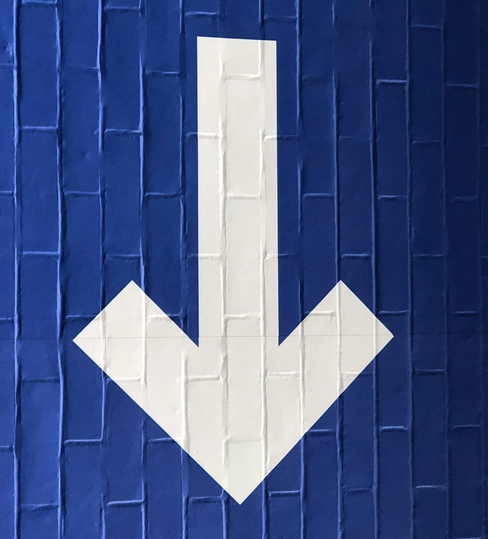 White downward arrow on a blue brick wall background.