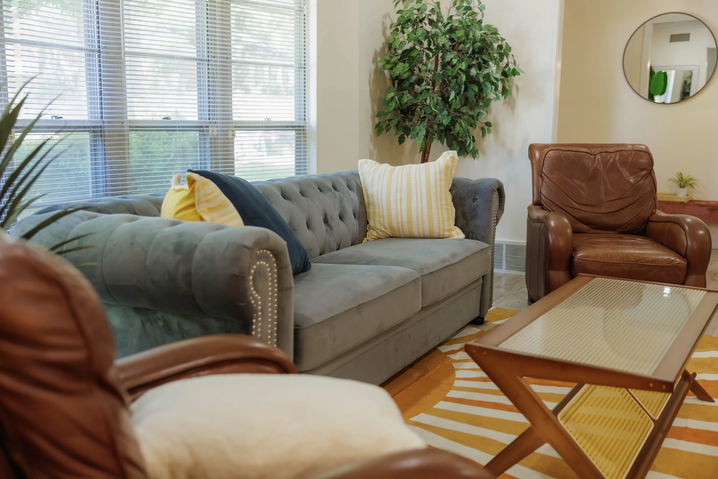 Cozy bed with white linens and three accent pillows in orange, cream, and teal tones inside a furnished midterm rental by Odyssei Solutions.