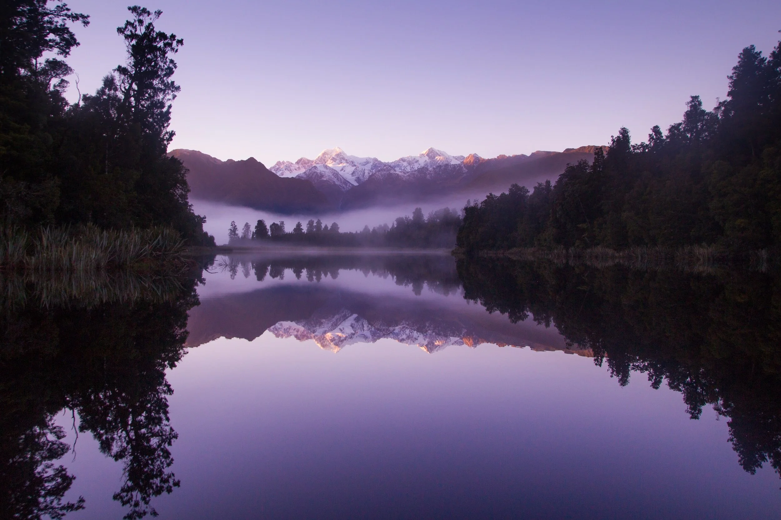 purple mountains and trees reflecting in lake