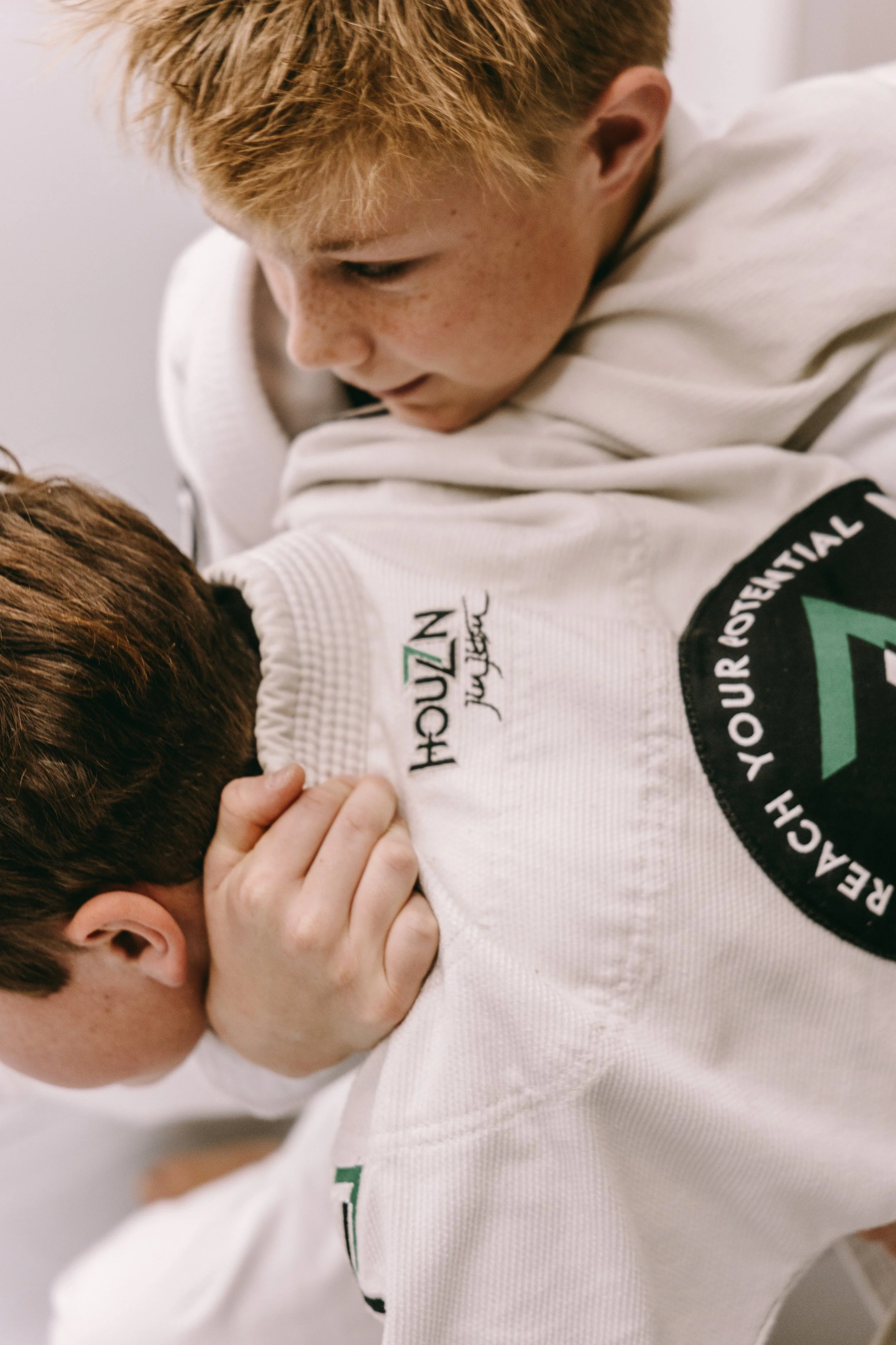 Close-up of two kids practicing a Brazilian jiu jitsu side control drill in white gis.