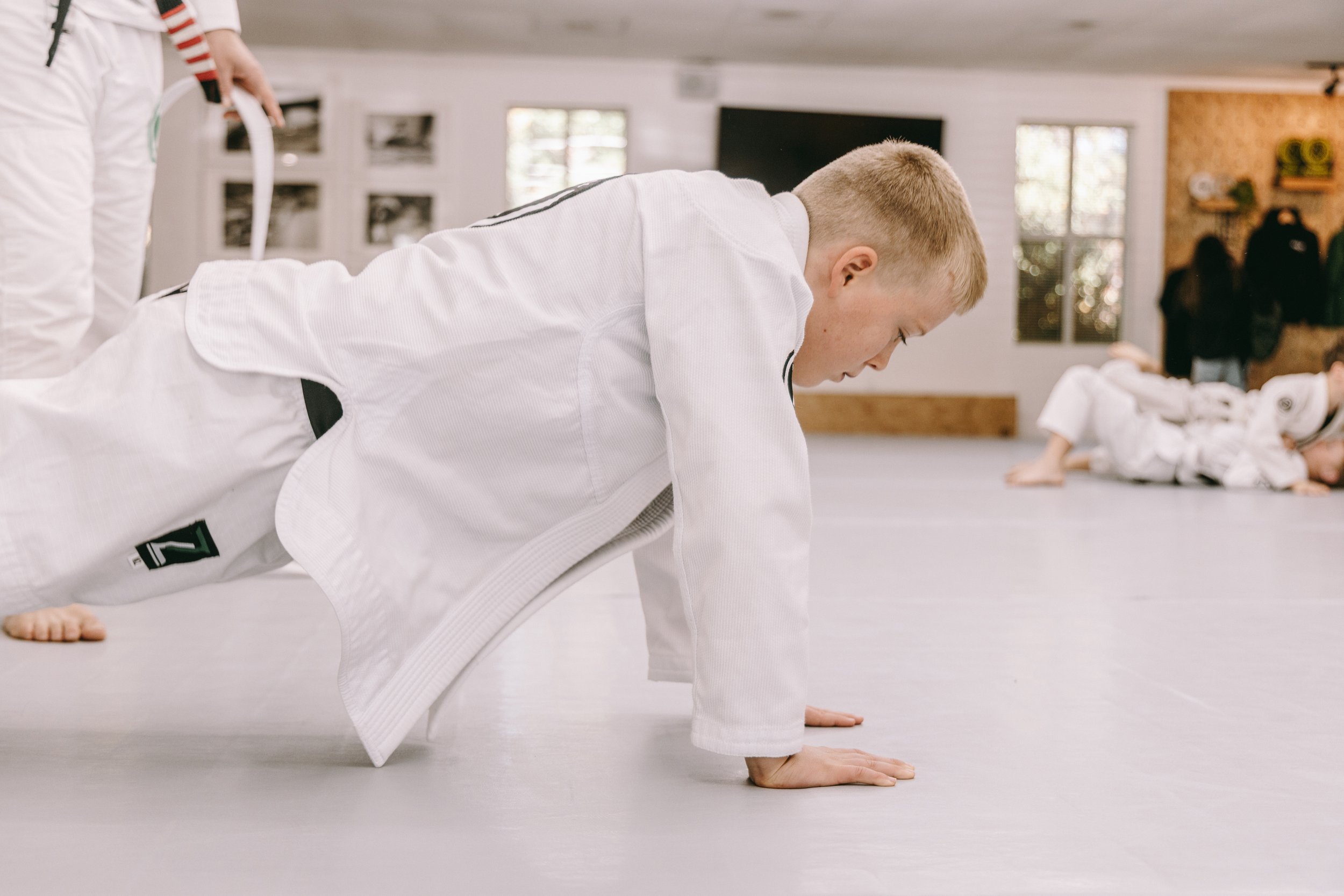 Child in a white gi does a bear crawl warm-up drill during a kids jiu jitsu class.