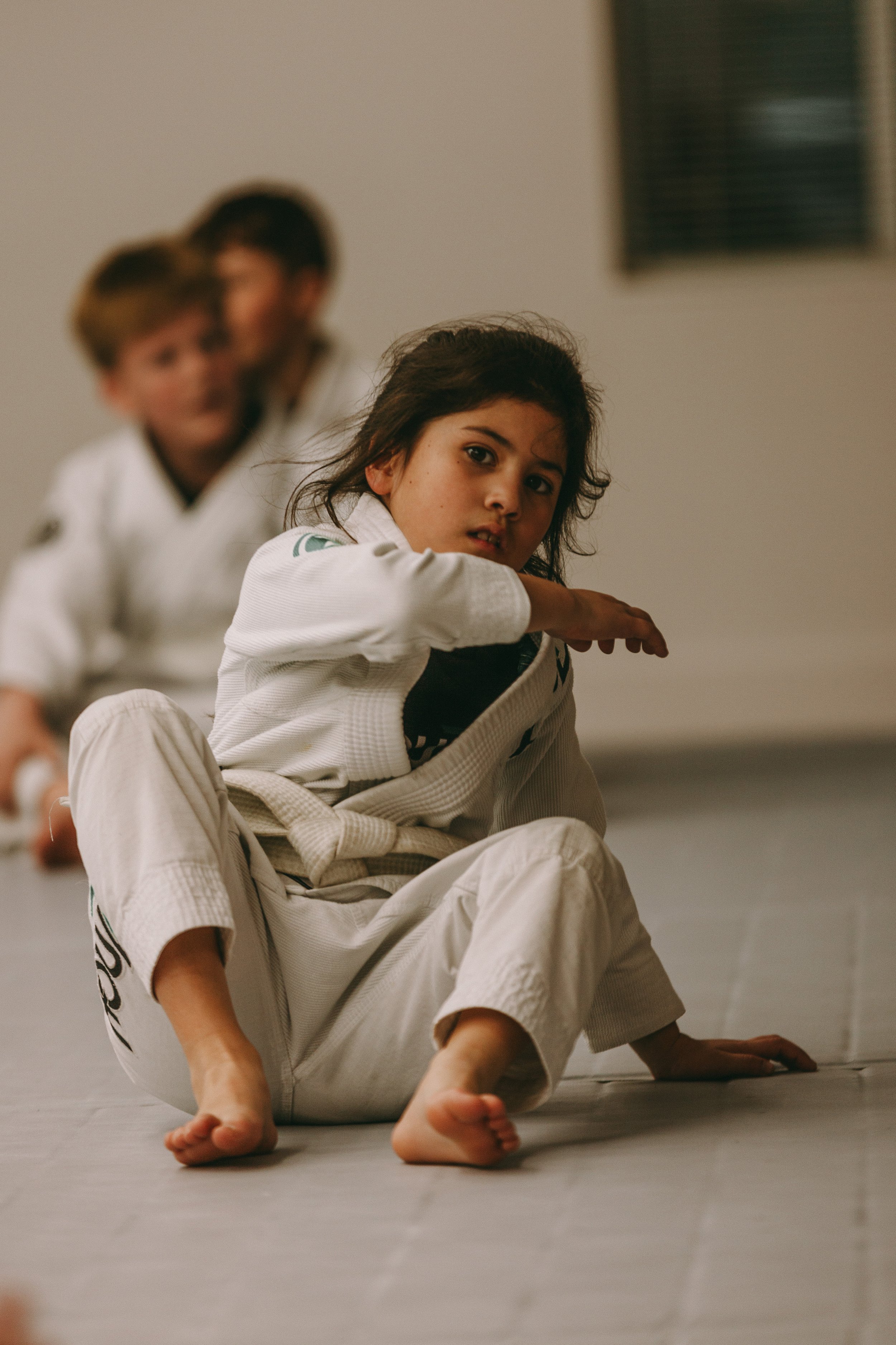 A young student in a white gi practices a jiu jitsu position with a partner at Houzn Jiu Jitsu Academy.