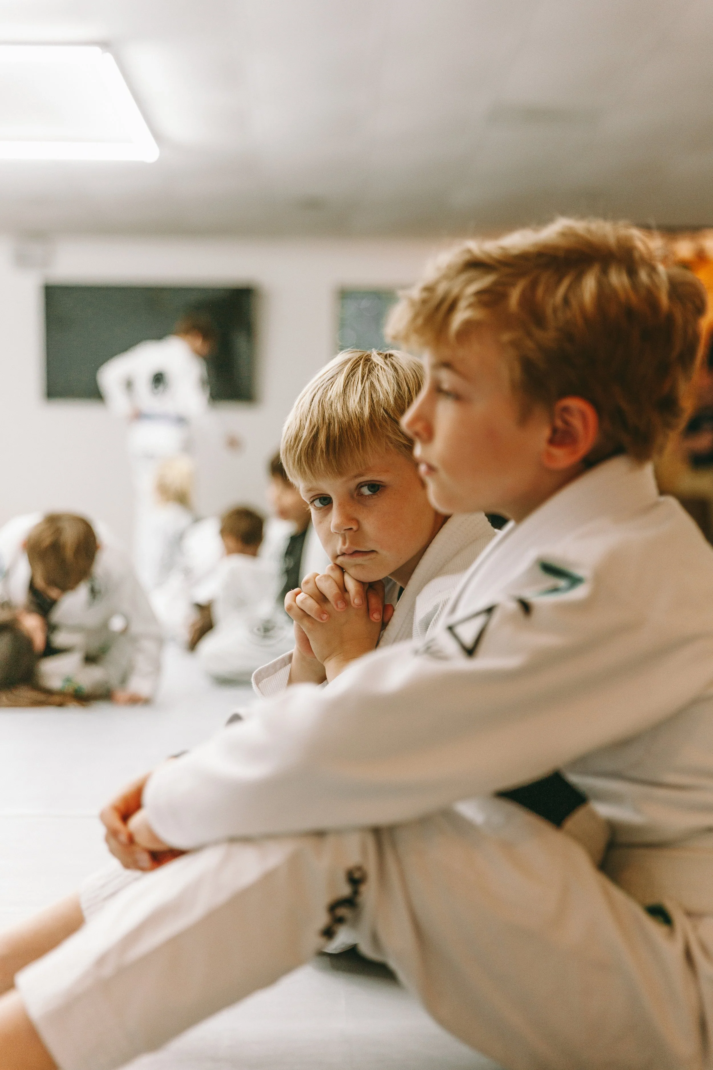 Young child in a kids Brazilian jiu jitsu class at Houzn Jiu Jitsu Academy sitting on the mat in a white gi during instruction