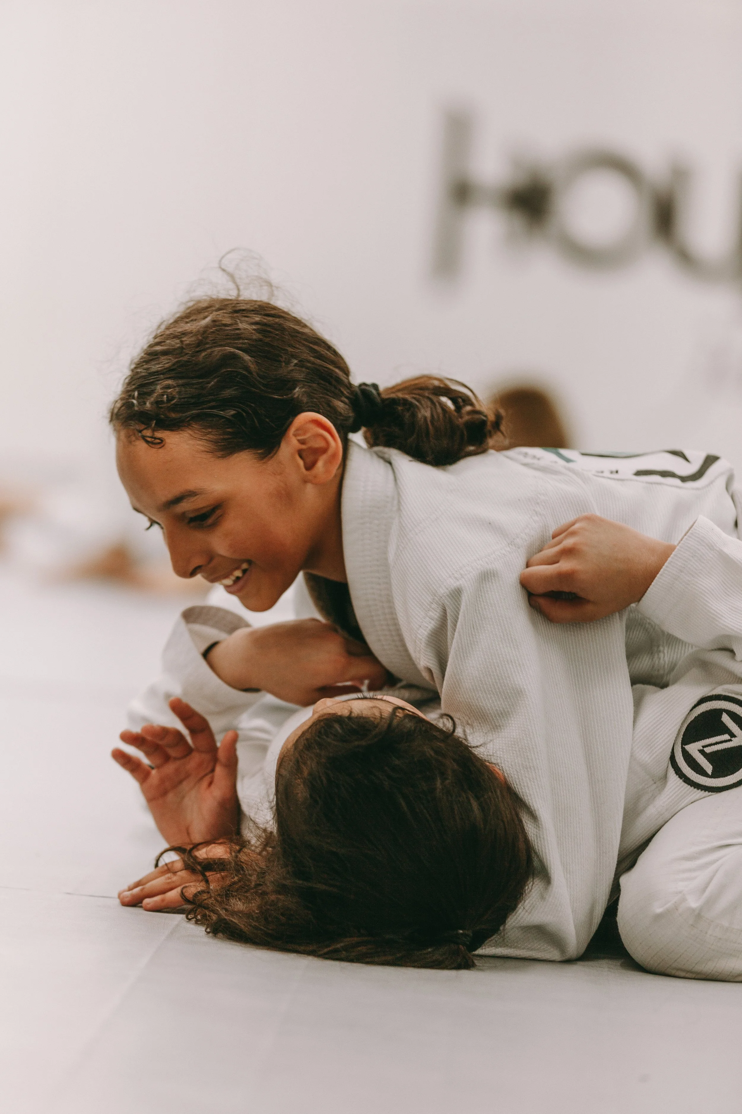 Two girls training Brazilian Jiu Jitsu during kids class at Houzn Jiu Jitsu Academy, practicing control and safe grappling on the mats.