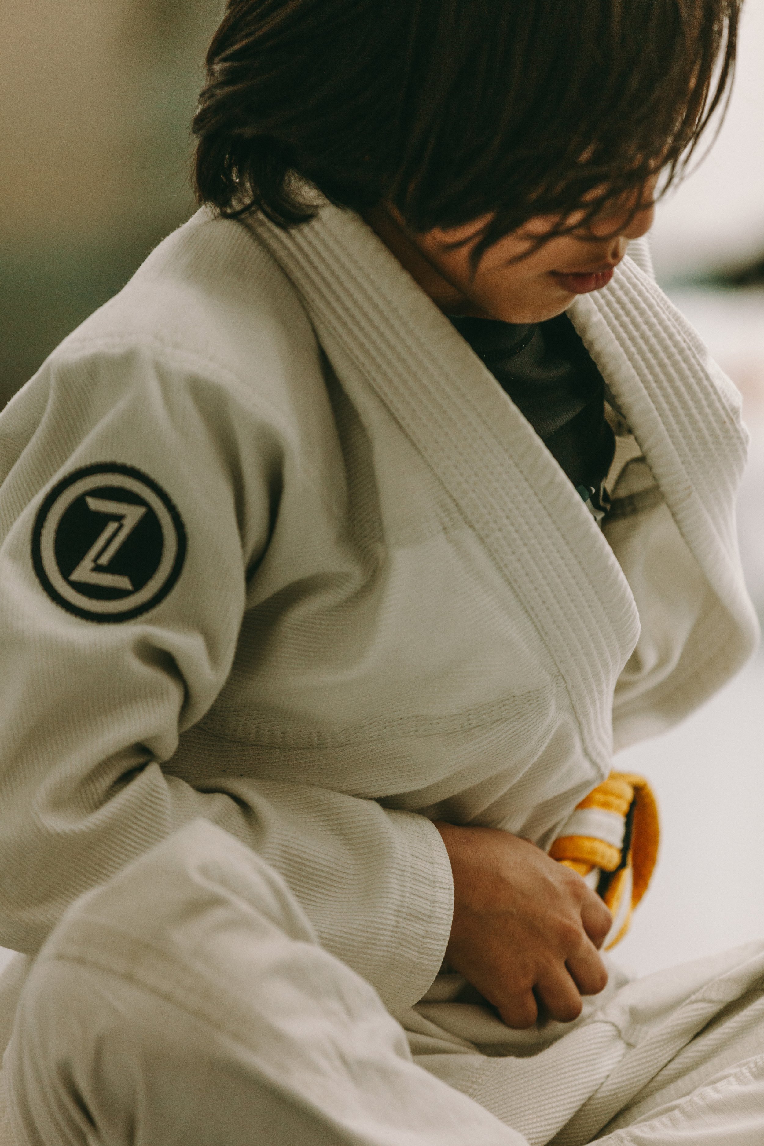 Close-up of a child in a white gi tying a yellow belt before Brazilian jiu jitsu class.
