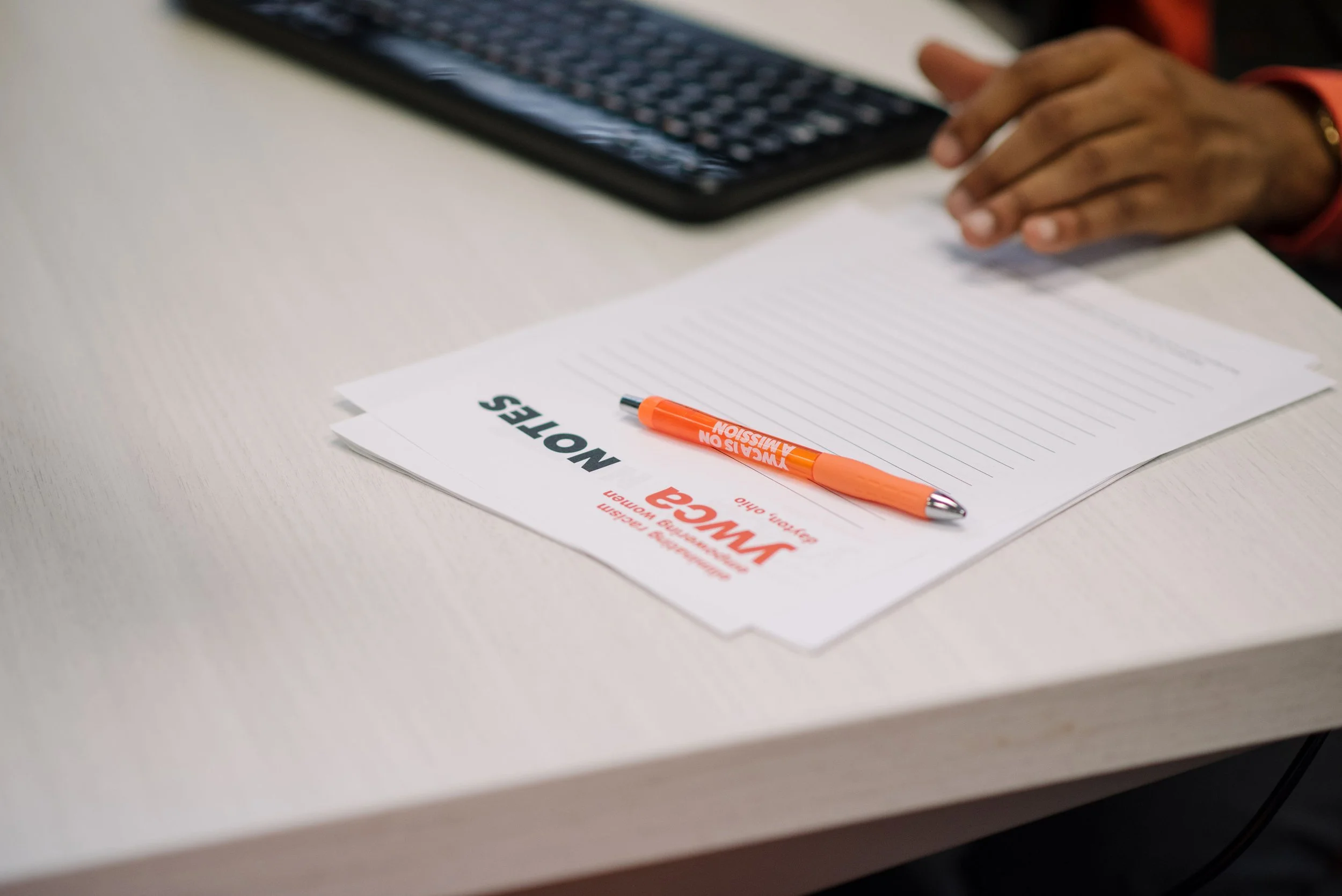 paper, keyboard and pen on table with a hand