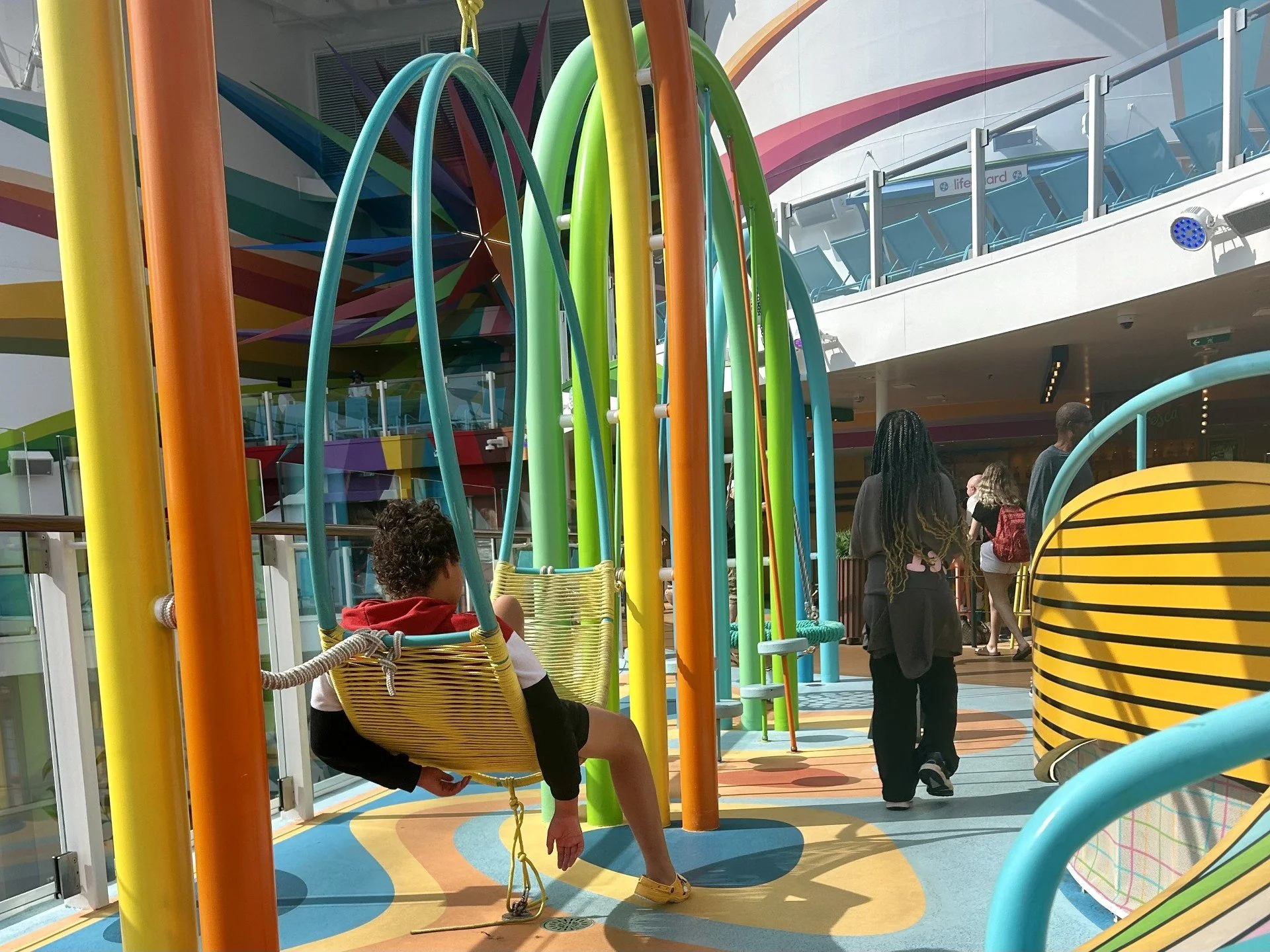 Colorful children’s play area with swings, climbing structures, and pathways on a cruise ship deck.