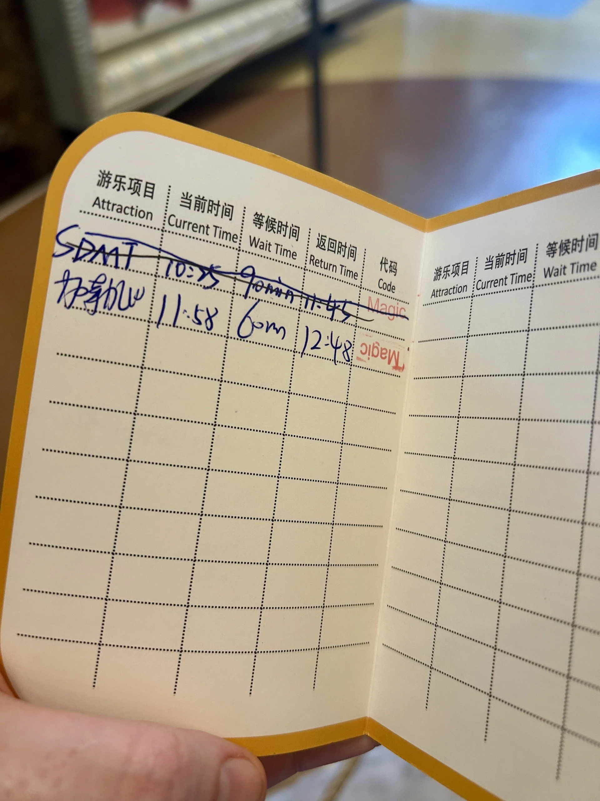 A printed and handwritten ticket or schedule with columns for attraction, current time, wait time, and return time, with handwritten notes indicating times and notes in both English and Chinese.
