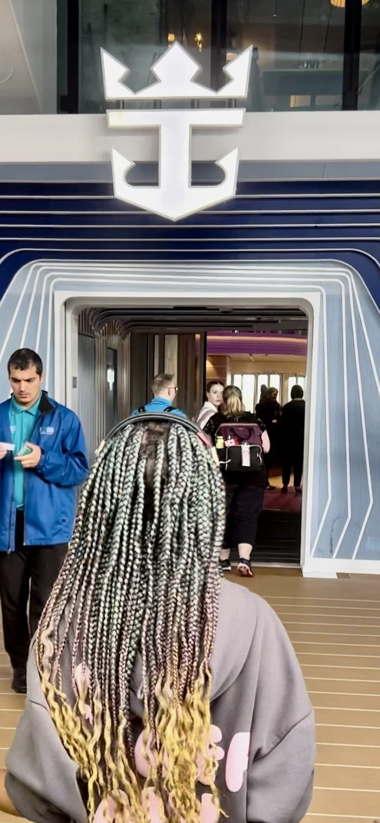 People walking inside a modern building with a prominent logo above the entrance, featuring a stylized crown and shield design.