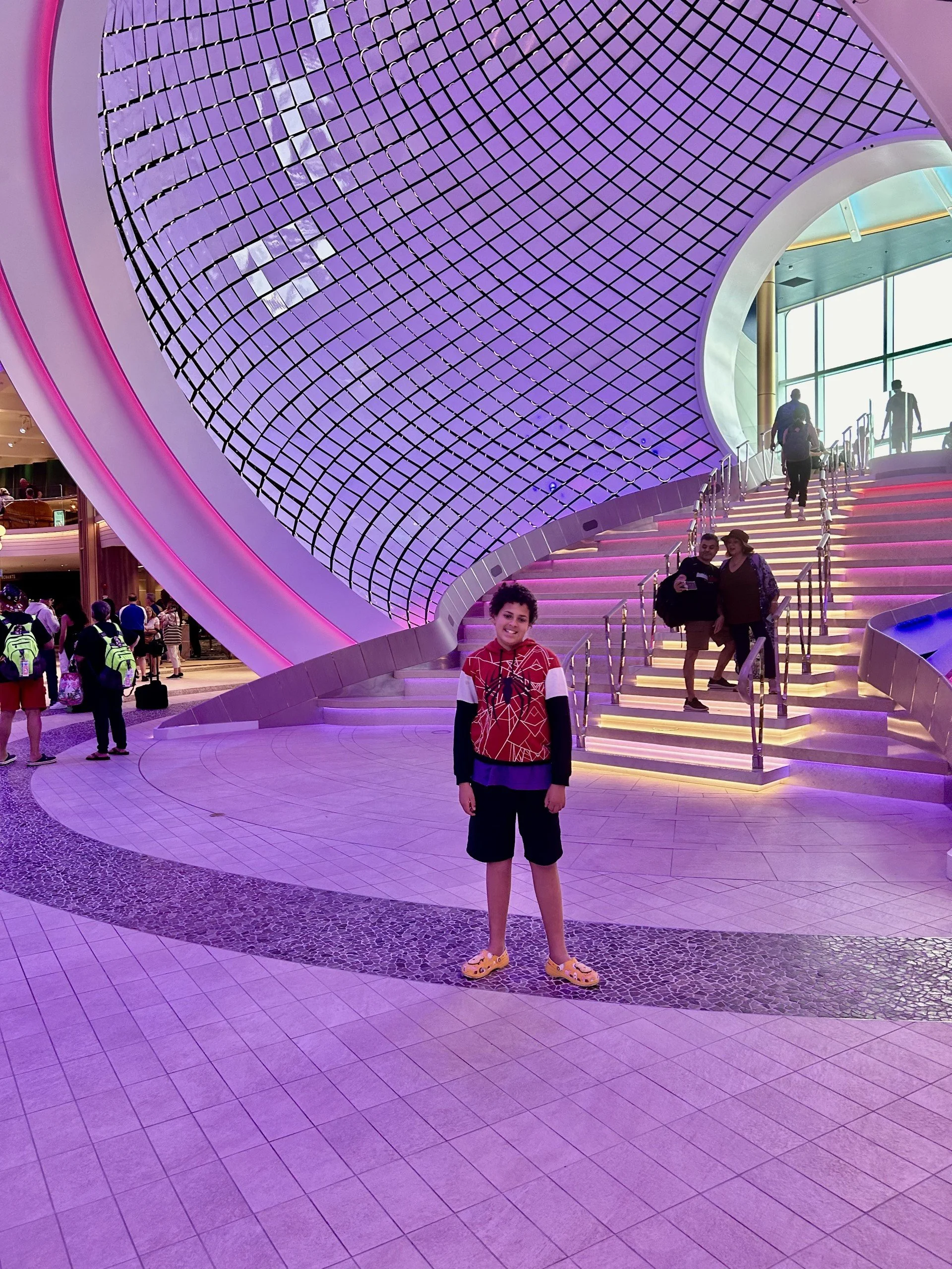 A young boy standing in front of a modern, colorful building with stairs and large windows. The architectural design features a curved structure with purple and pink lighting.