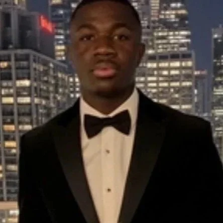 Young man in tuxedo with bow tie standing outdoors at night with city skyline in background