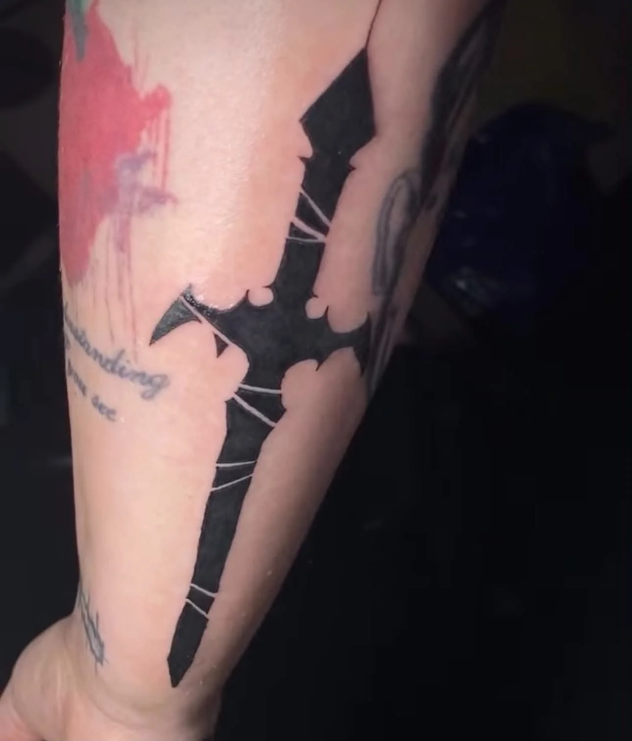 Close-up of a person's arm with a tattoo of a black silhouette of a man's face and neck, along with some handwritten text.
