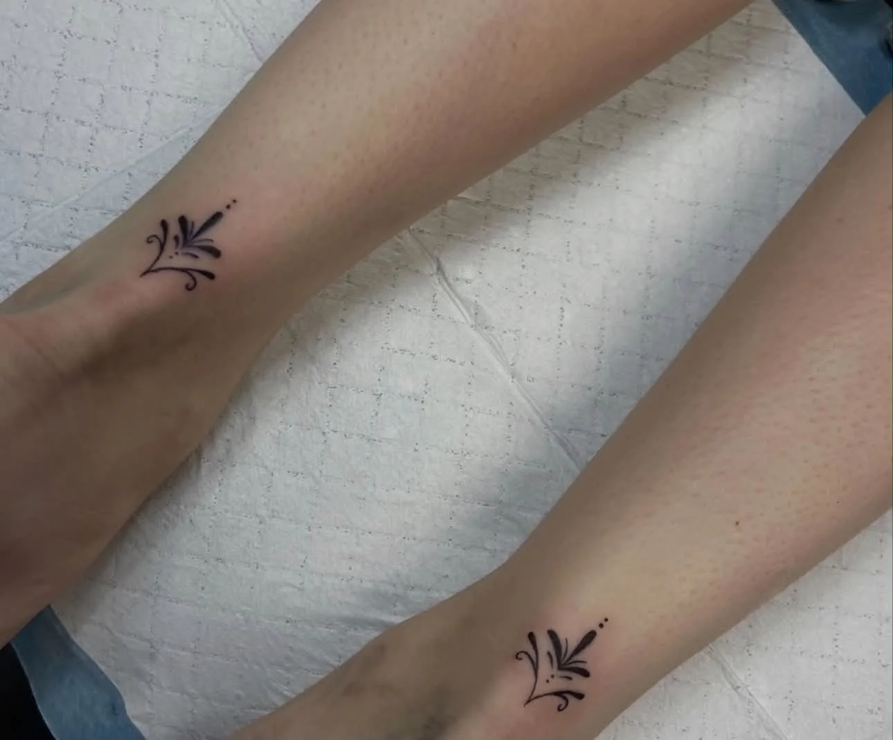 Tattoo of a decorative floral design on person's forearms, with a simple black ink pattern featuring curved lines and small dot accents.