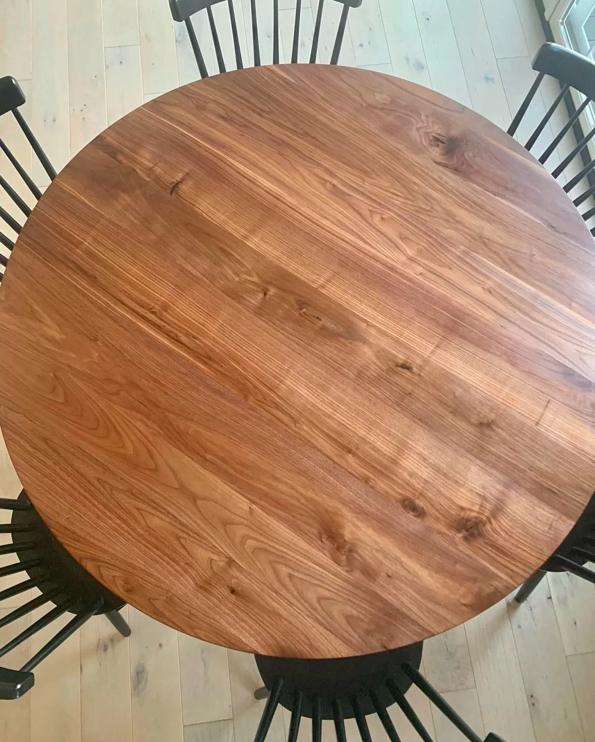 Round wooden dining table with black chairs on a light wood floor