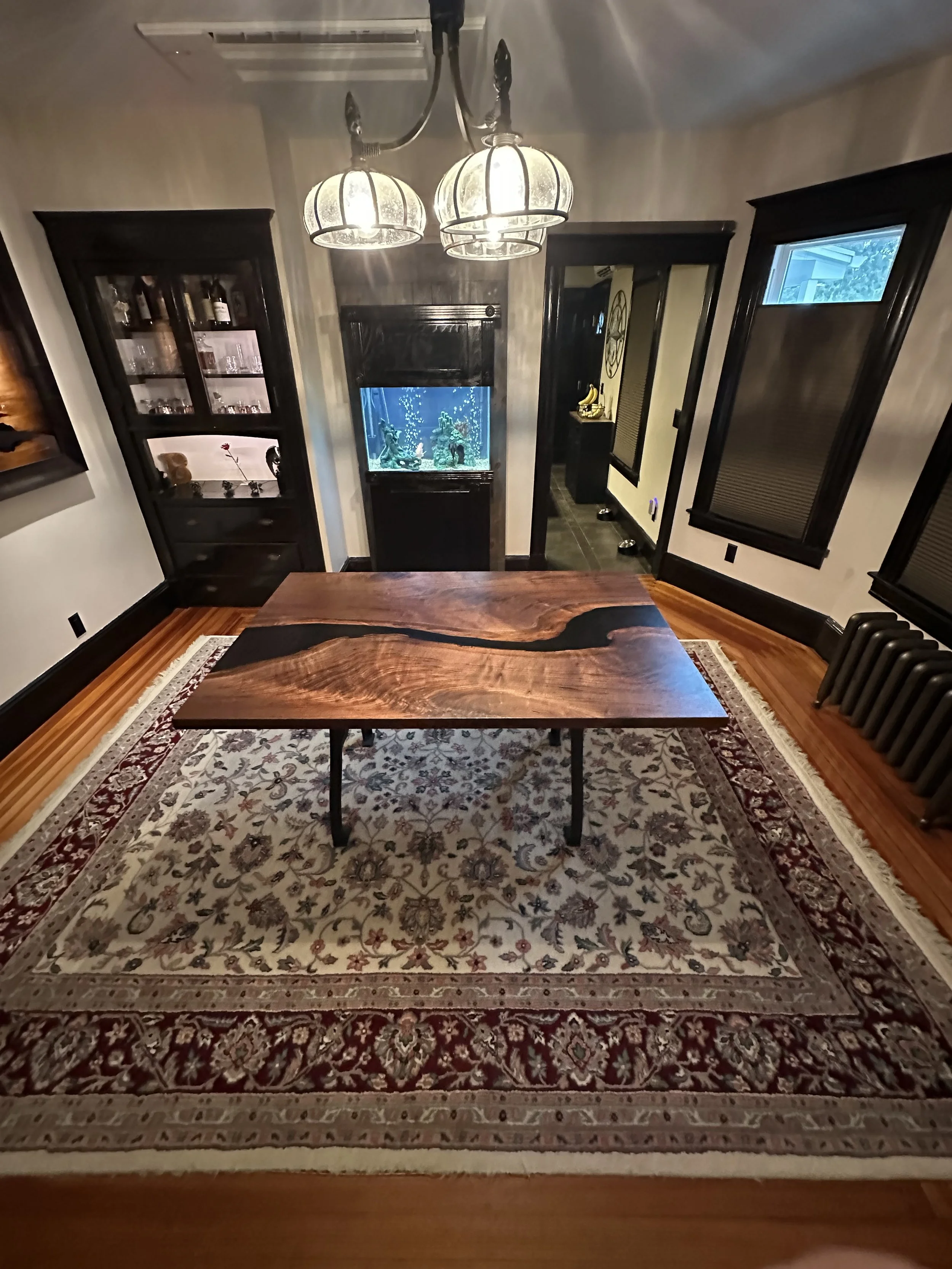 A dining room with a rectangular wooden table on a decorative area rug, black wooden cabinets, a fish tank, and windows with black trim.