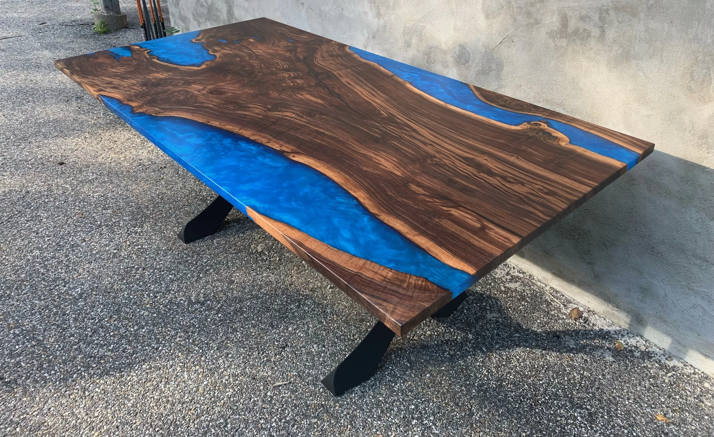 Live edge wood table with blue epoxy resin on metal legs outdoors