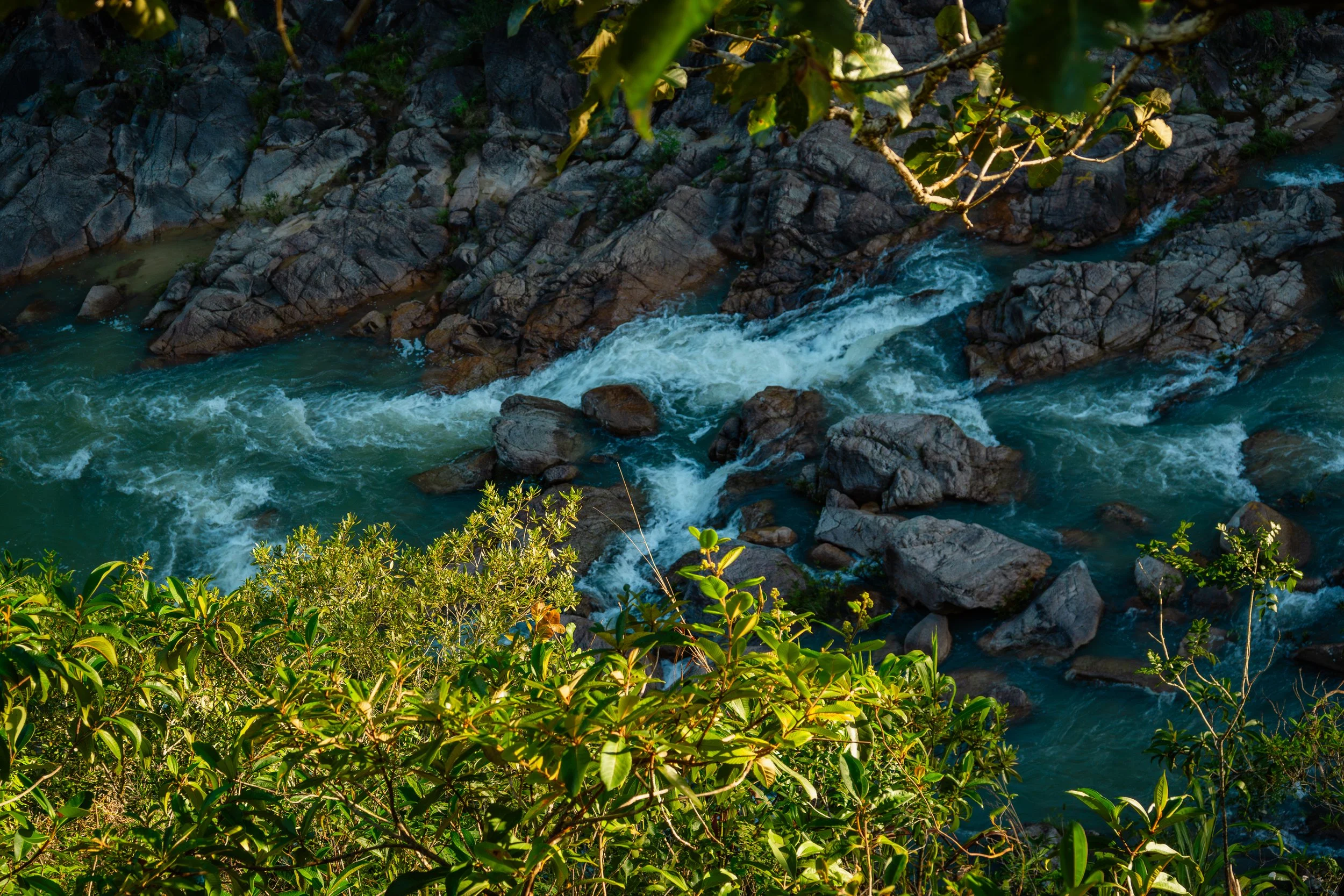 Under beautiful lighting, three women savor a buffet lunch atop an inverted kayak, set against the river’s edge with sweeping mountains and the river stretching behind them.