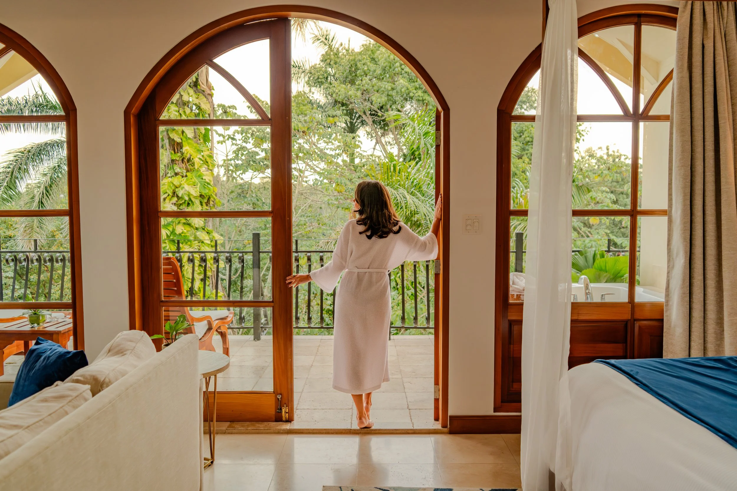 A guest standing in the open doorway of a private balcony at San Ignacio Resort Hotel, overlooking the dense tropical jungle canopy of the Macal River valley.