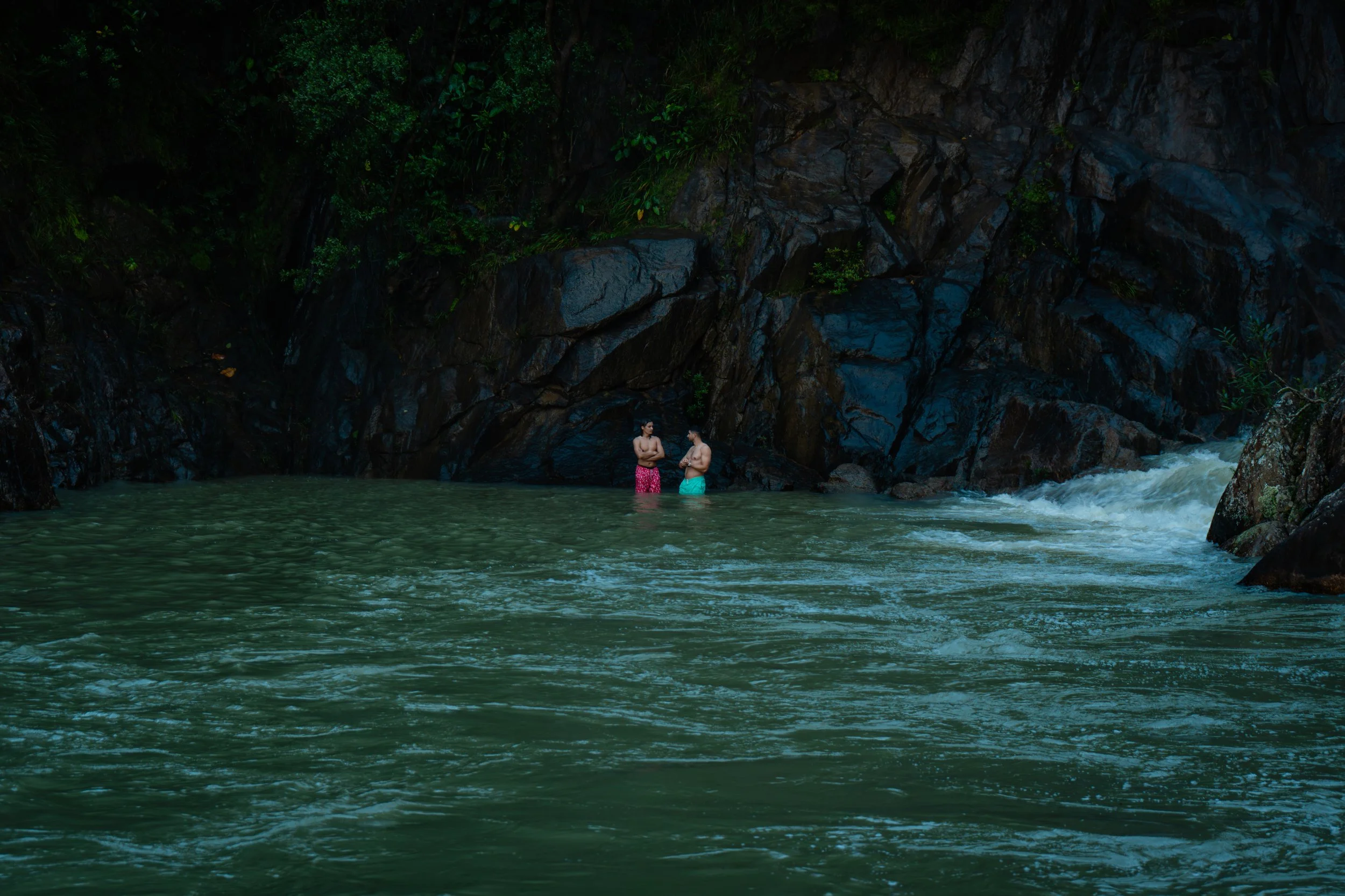 Lush green tropical rainforest with fog rolling over it and distant mountain ranges under a pink and purple sky.