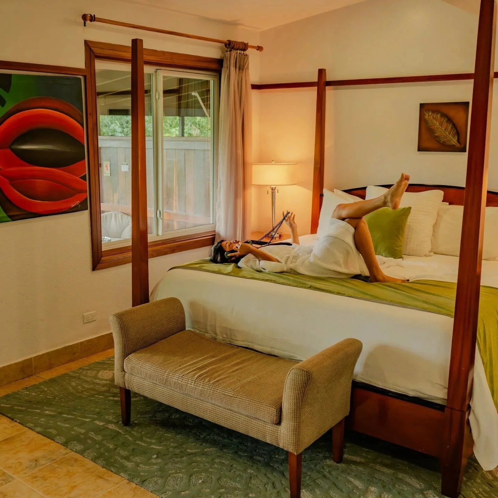 A guest lounging on the bed in a River View Suite at San Ignacio Resort Hotel while ordering coffee, highlighting the spacious room layout and elegant interior design.